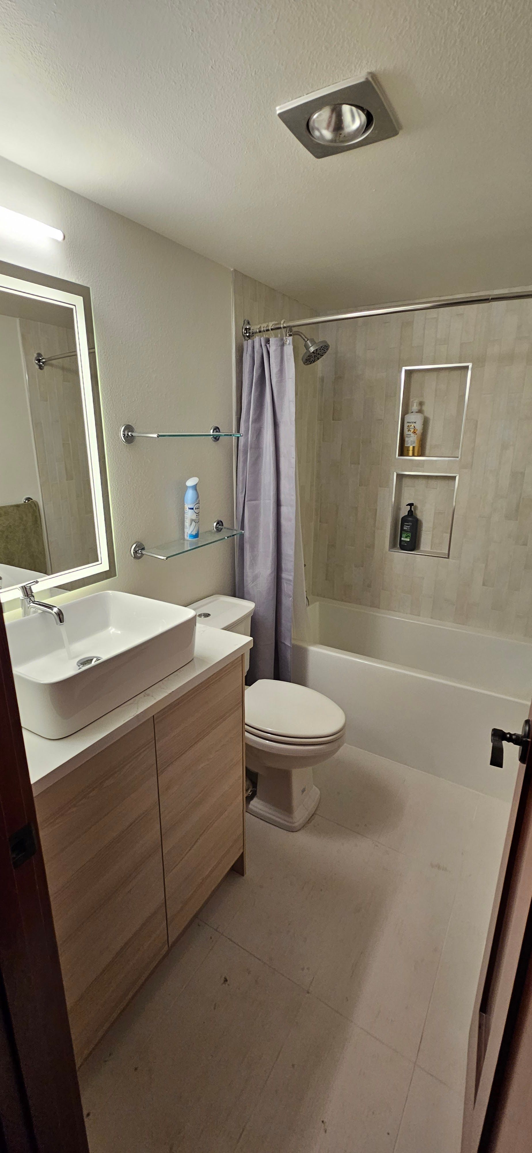 Bathroom with a vanity, toilet, and shower/tub. Beige tile, wooden vanity, white sink, and light gray shower curtain.