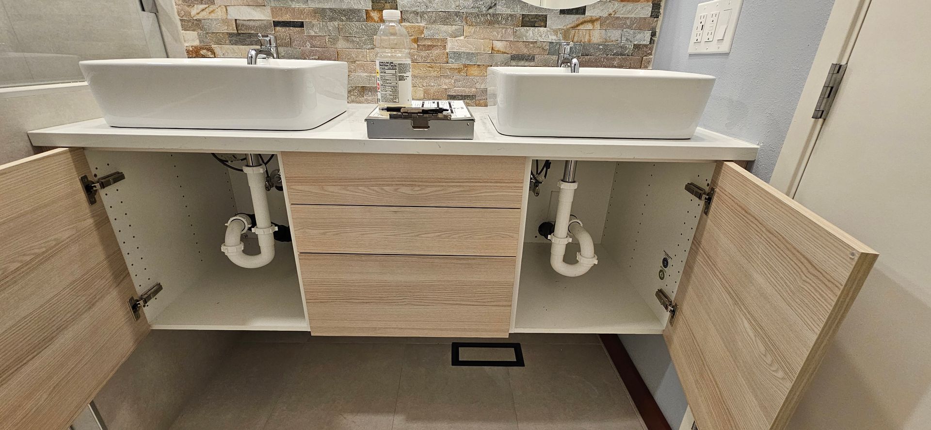 Bathroom vanity with two white sinks, wooden cabinets, and a stone tile wall.