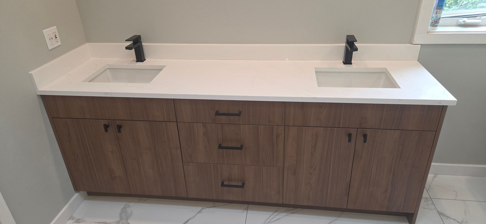 A brown bathroom vanity with two sinks, black faucets, and a white countertop.