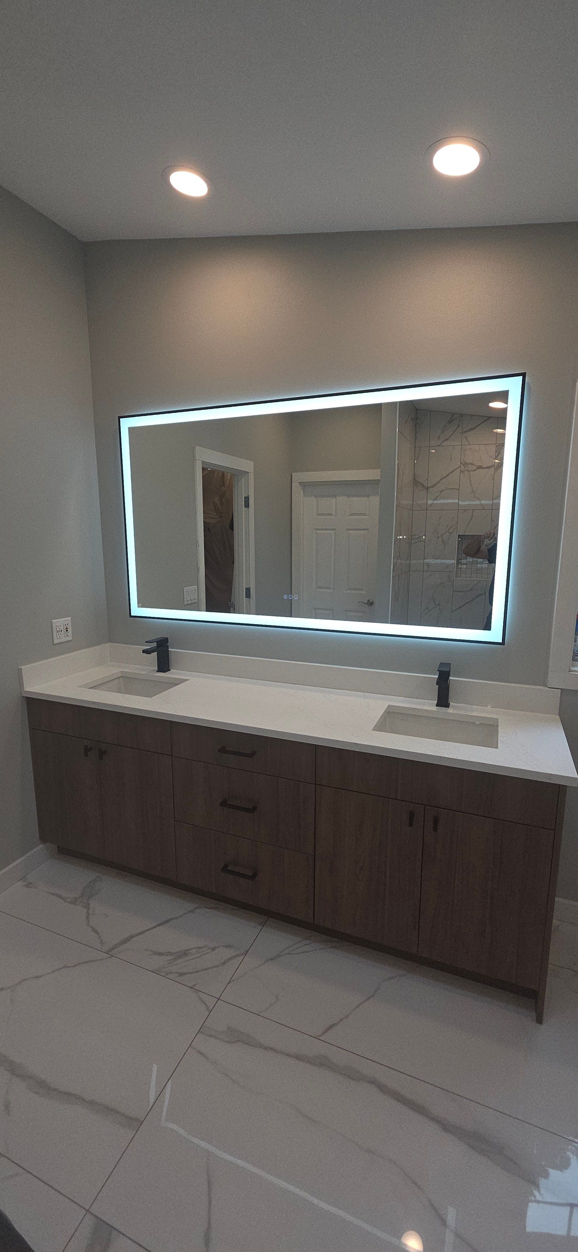 Modern bathroom with a large mirror with LED lighting, a double sink vanity, and tile floors.
