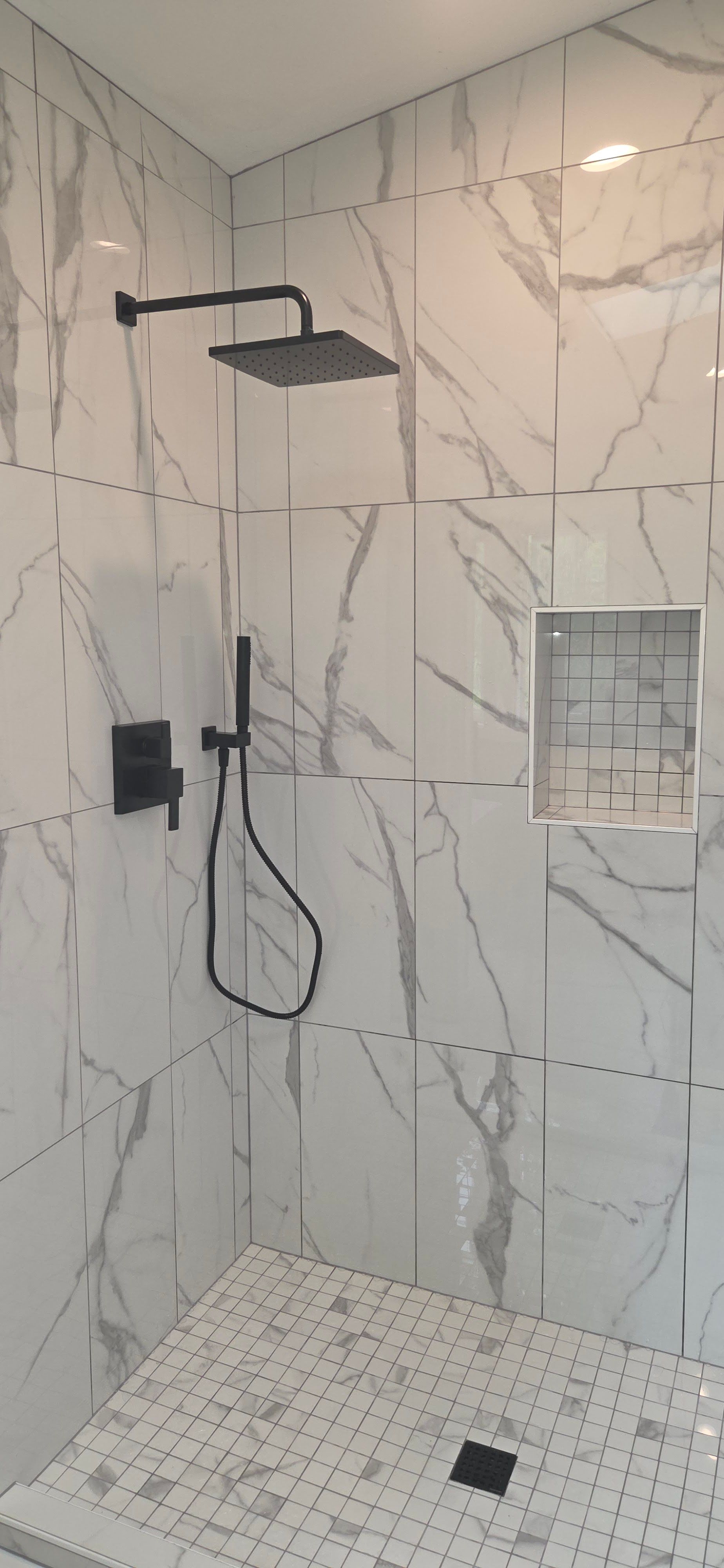 A shower with black fixtures and white marble-patterned tiles.