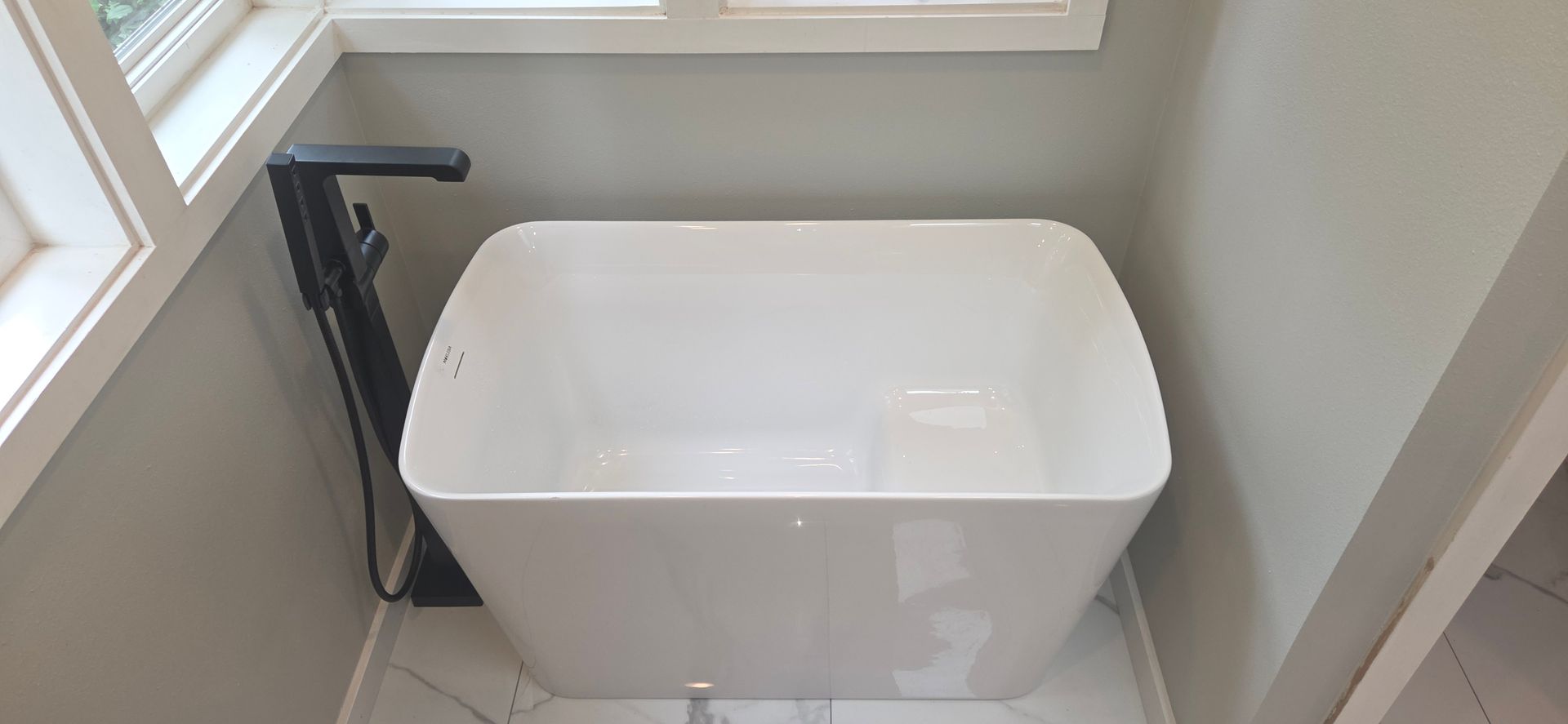 White square bathtub in a bathroom, with black faucet and window above.