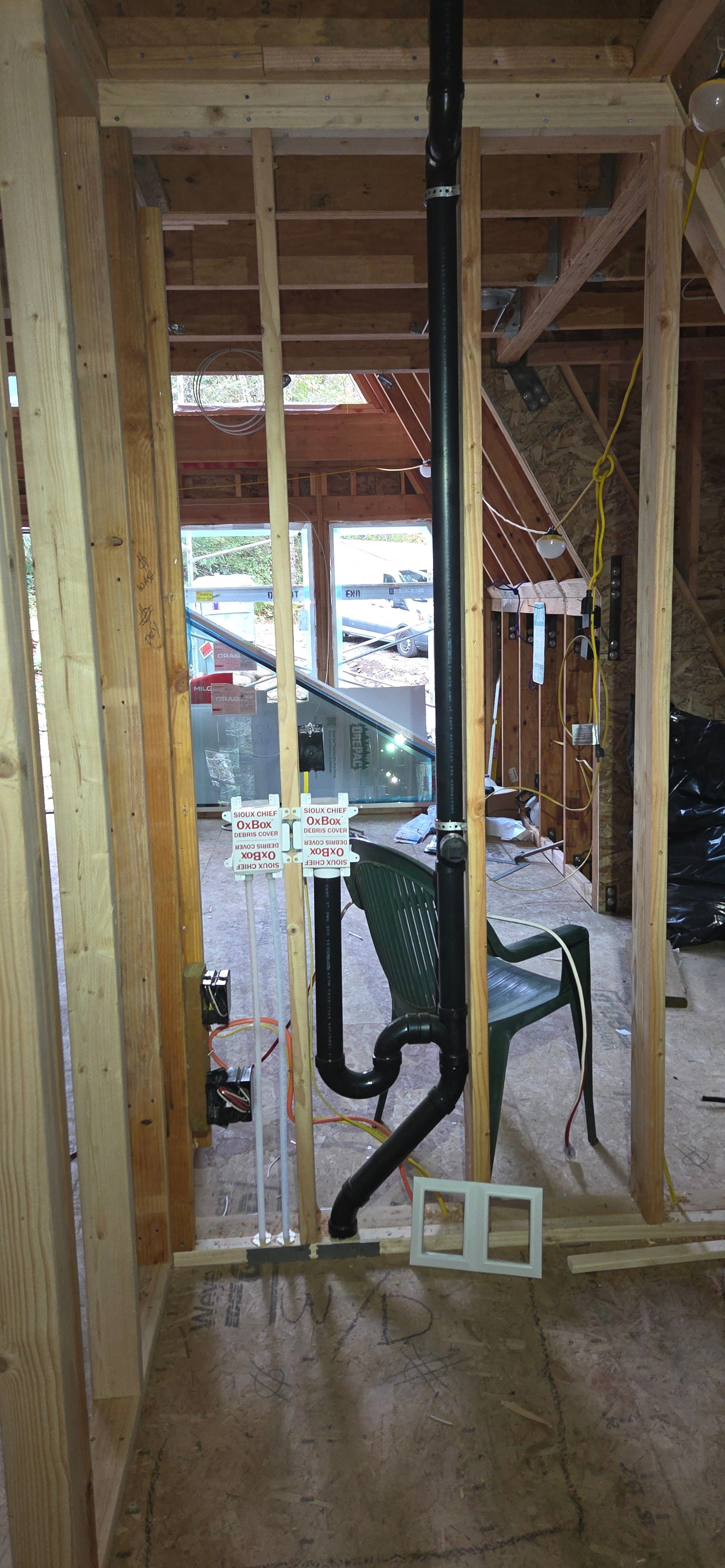Interior view of a building frame with plumbing pipes and an electrical box installed.