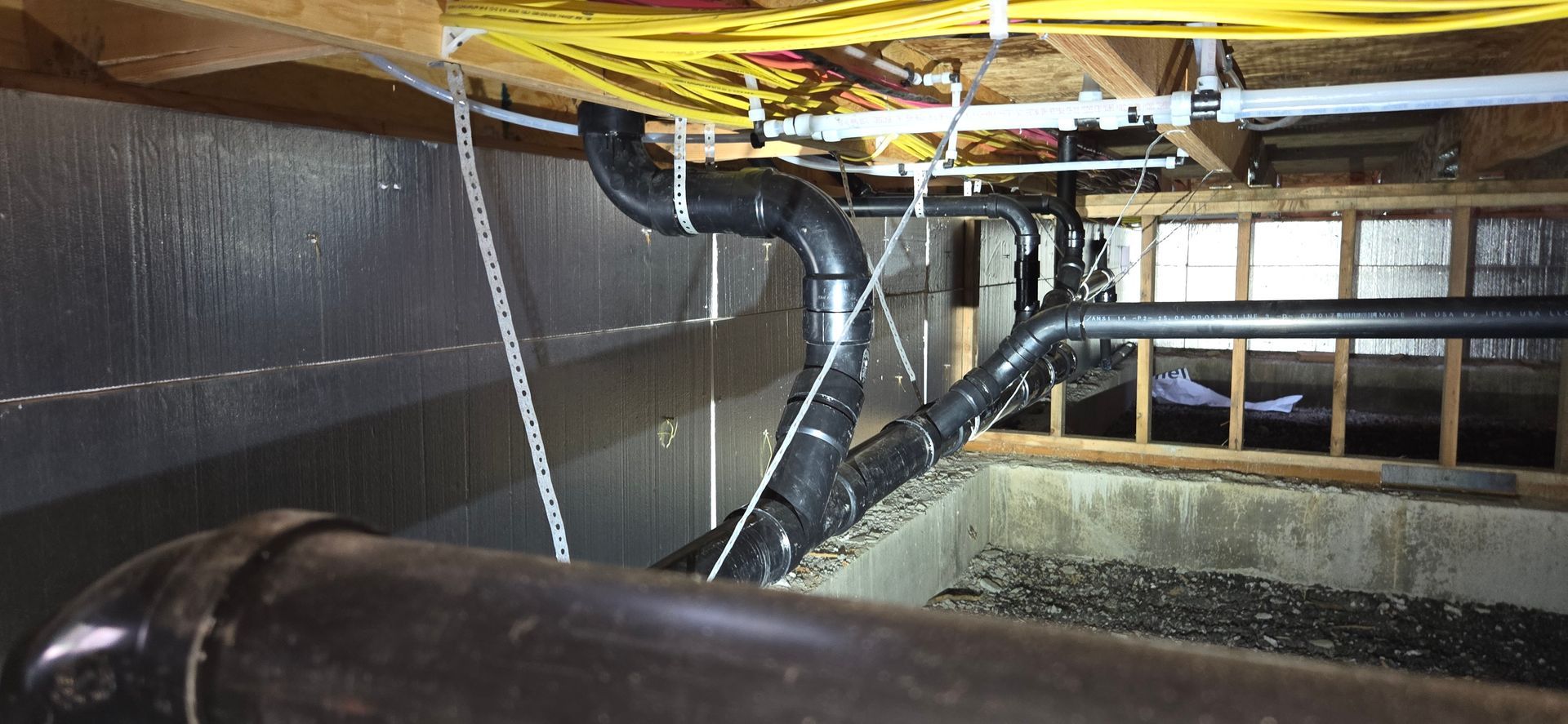 Black pipes in a crawl space, secured to the ceiling with plastic ties.
