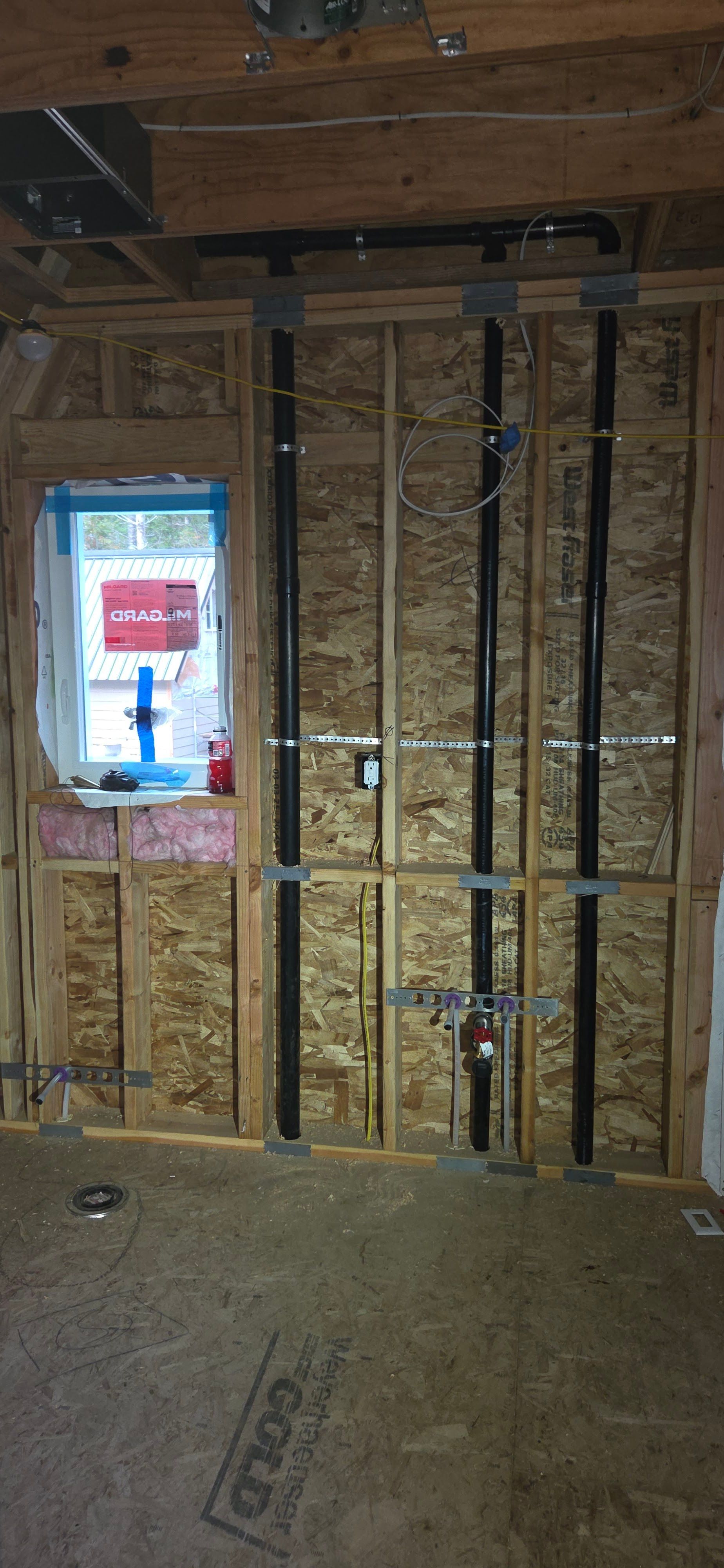 Interior view of a construction site showing exposed plumbing pipes running vertically along a wall.