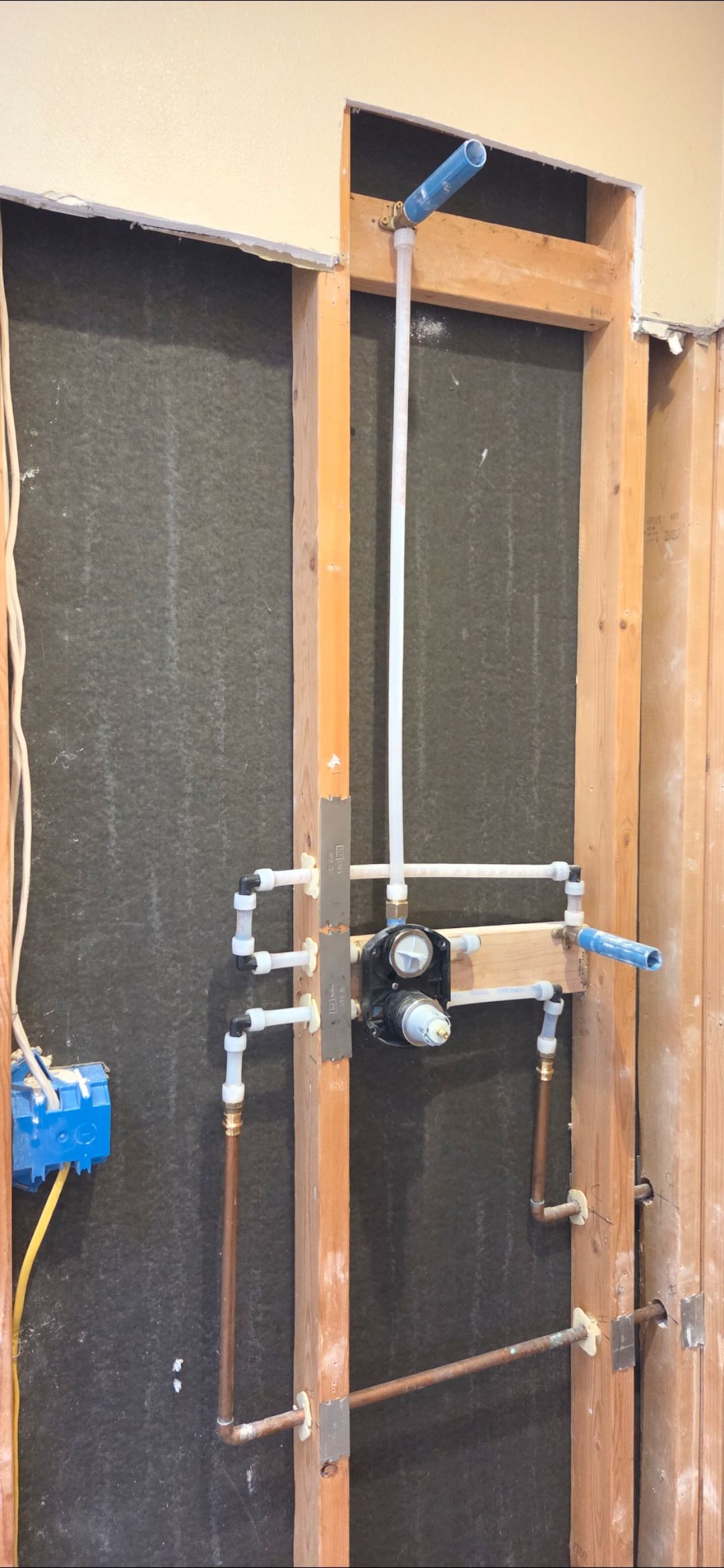Shower plumbing installed in a wall. Copper pipes, valves, and a shower arm are visible.