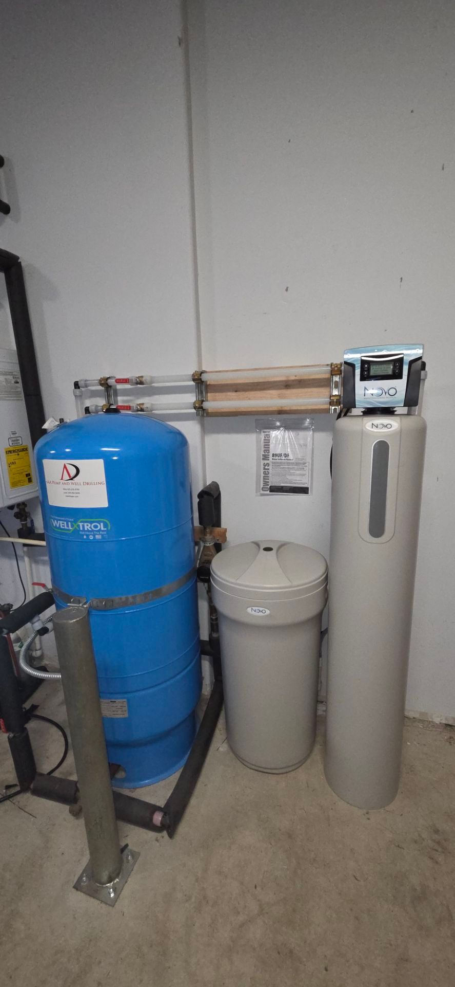 Water filtration and pressure tank system in a utility room. Blue, beige and gray components.