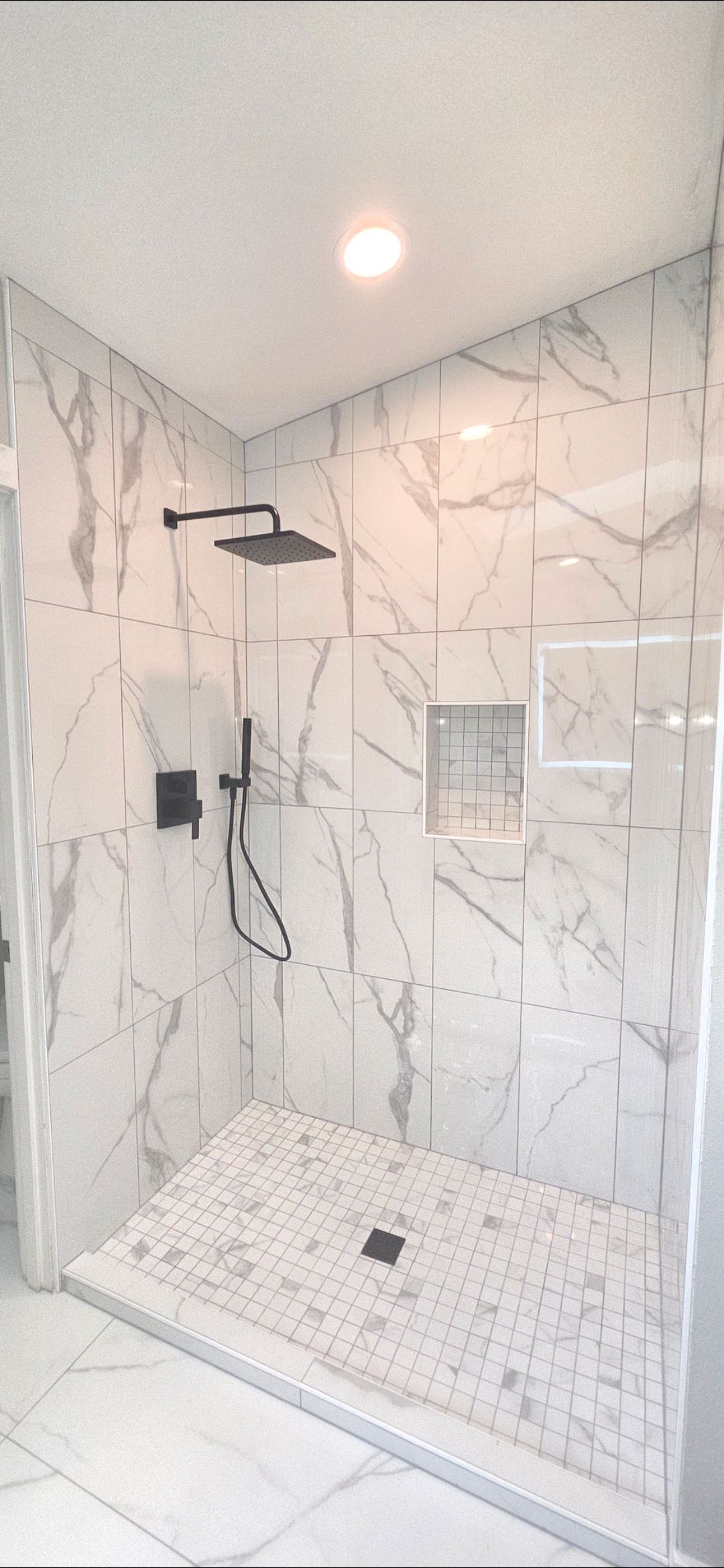A marble-tiled shower with a black showerhead, fixtures, and a recessed shelf.