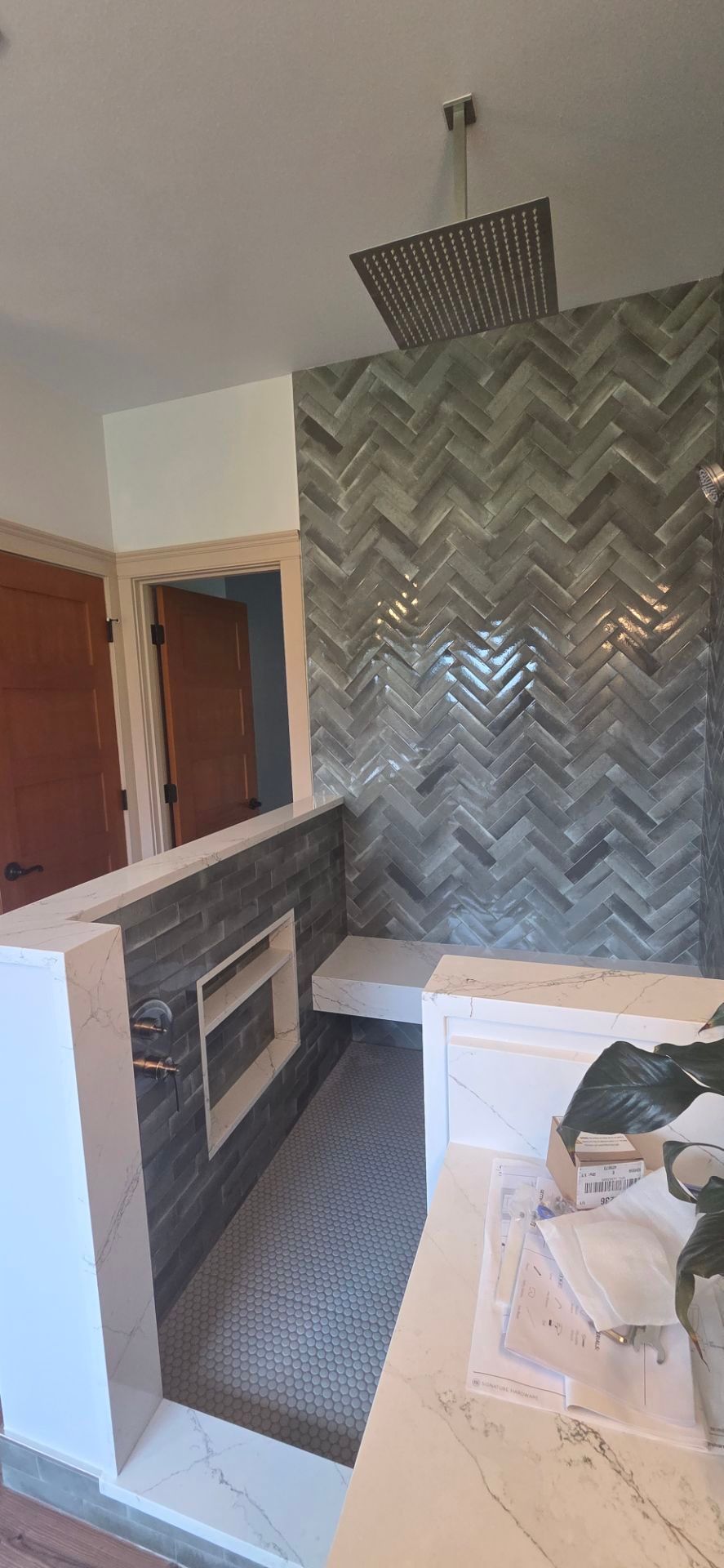 Shower with herringbone tile wall, bench, and square showerhead.