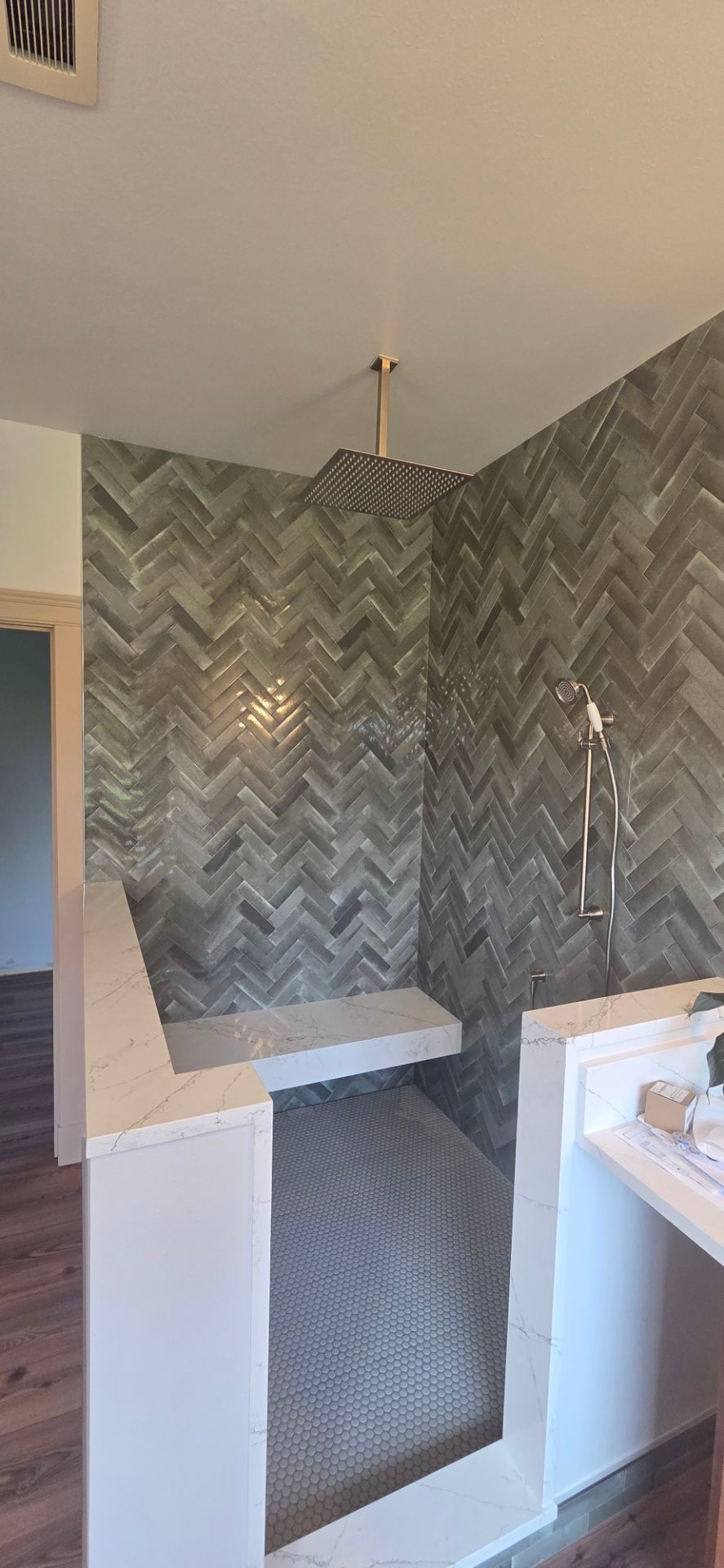 A tiled shower with a built-in bench. The walls feature a gray chevron pattern, with gold shower fixtures.