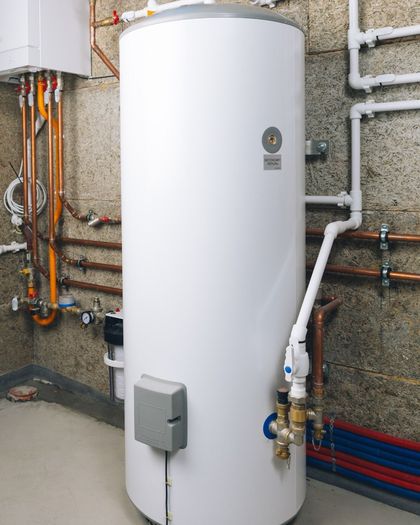 White water heater in a basement with copper and plastic pipes.