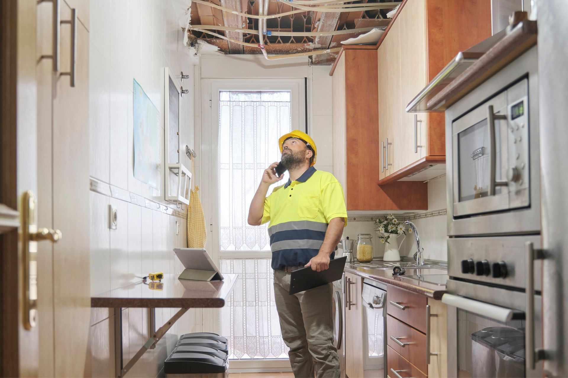 A man is standing in a kitchen talking on a cell phone.