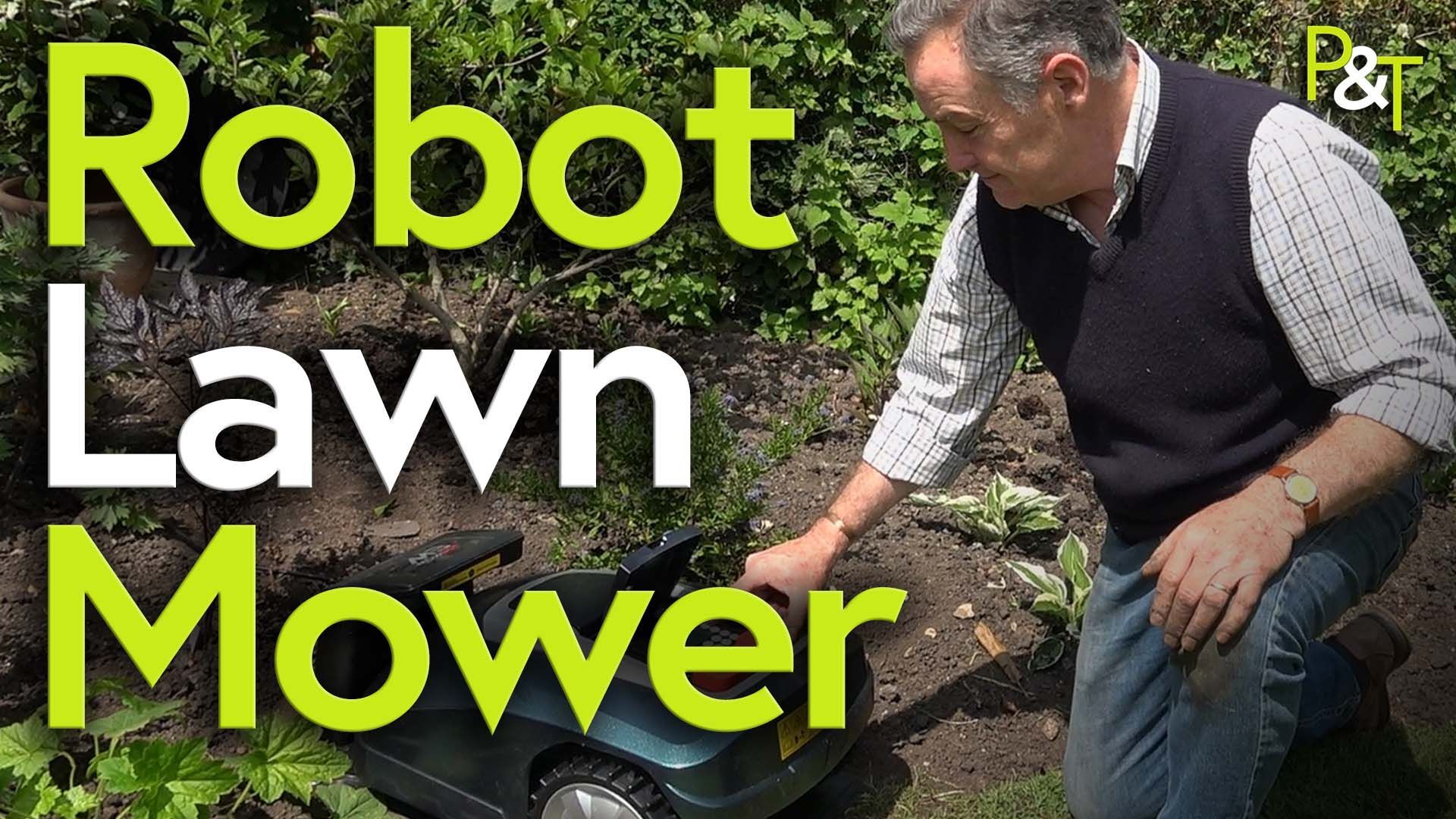 Martin Fish, gardener, to the right of frame shot slightly from above. He is leaning to his right over a robotic lawn mower in dark green - it's in its charging bay and behind him and it is a flower bed, so soil and some greenery. the text Robot Lawn Mower in green and White slightly obscure the lawn mower as they cover it on the left of frame.
