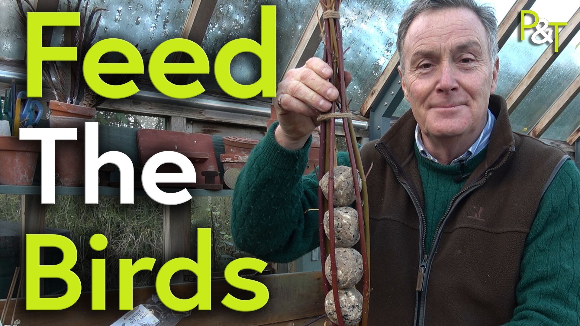 Martin Fish (right of frame) stands in a greenhouse holding up a home-made bird feeder comprising fat balls encased in dogwood pruning. The text Feed the Birds in green and white over the lefthand side of the image.