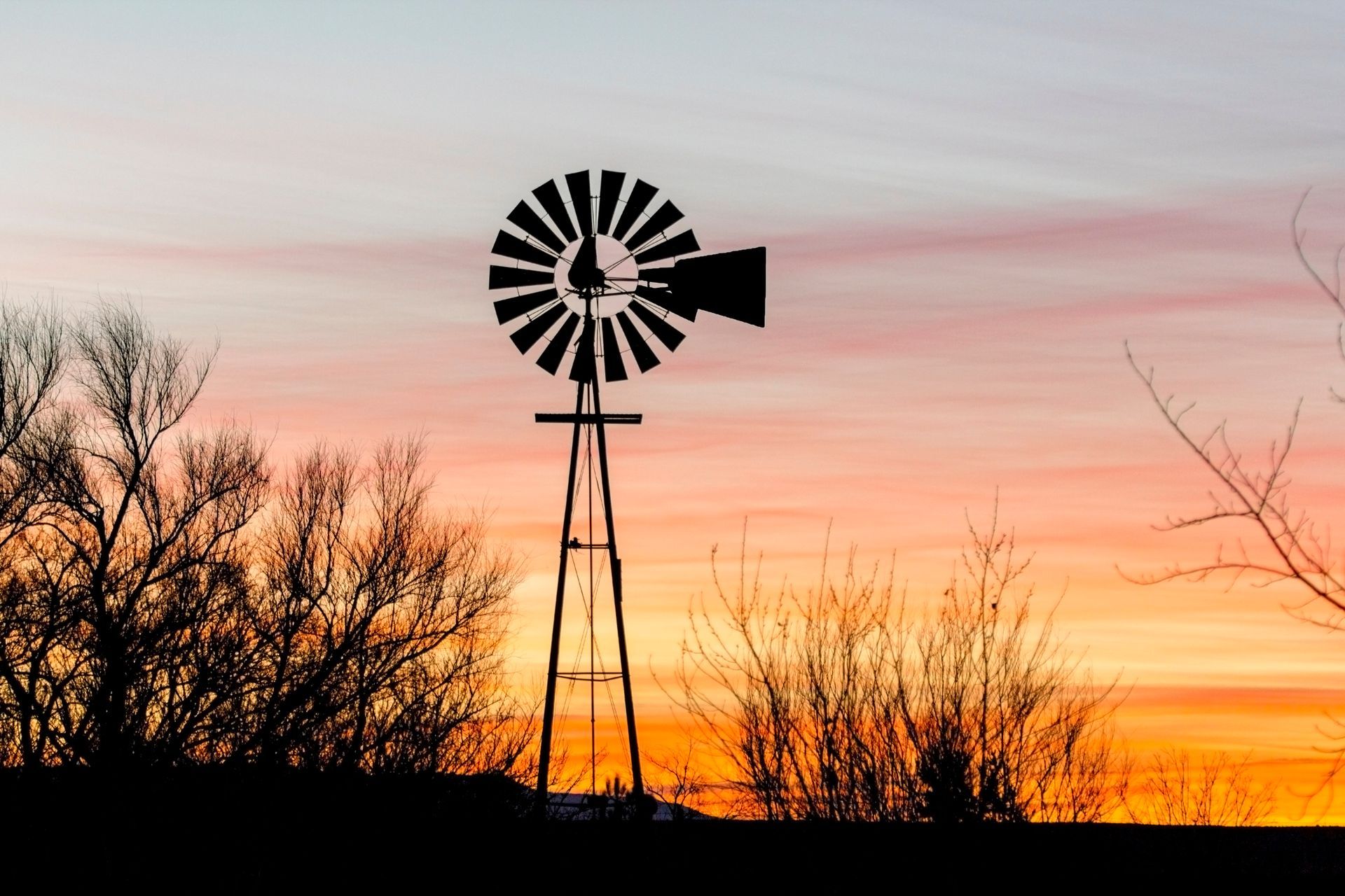 Silhouette of a windmill against a vibrant sunset with orange and pink hues.