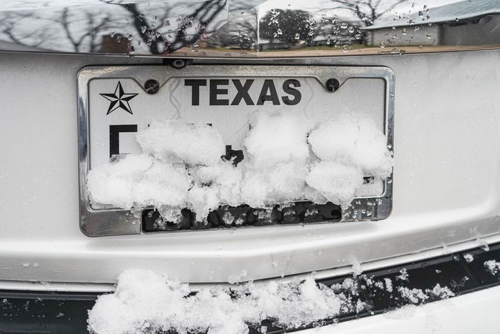 A texas license plate is covered in snow.