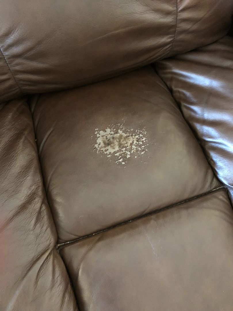 Brown leather couch seat with a patch of damaged leather in the center.