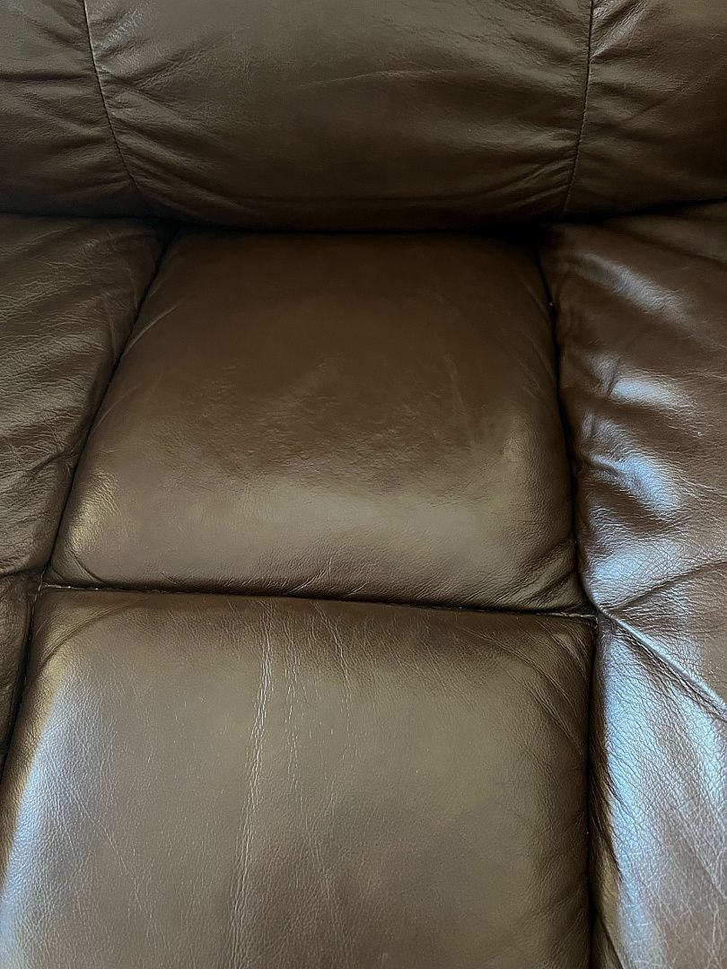 Brown leather couch with quilted cushions, showing wear and tear.