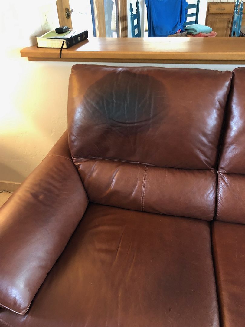 Brown leather sofa with a dark stain on the headrest.