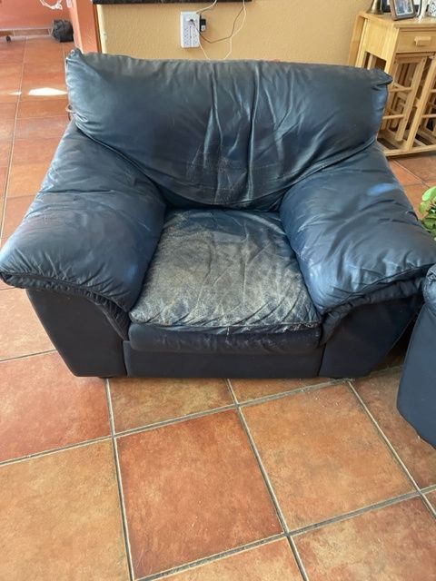 Black leather armchair on tiled floor; showing wear and tear.