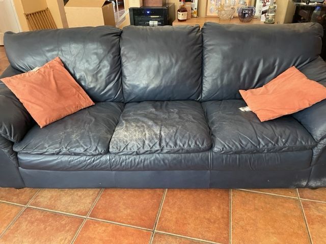 Dark blue leather sofa with orange cushions on a terracotta tile floor.