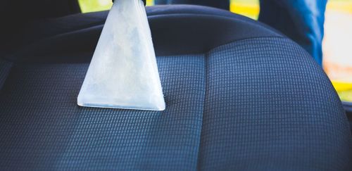 A person cleaning a car seat with a vacuum.
