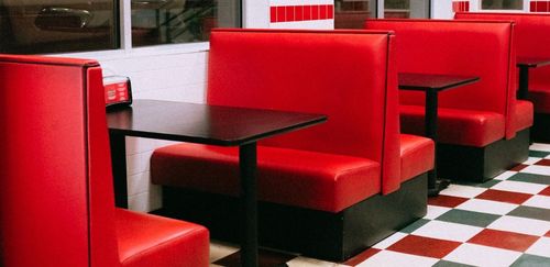 Red diner booths with black tables, on a checkered floor, inside a diner.