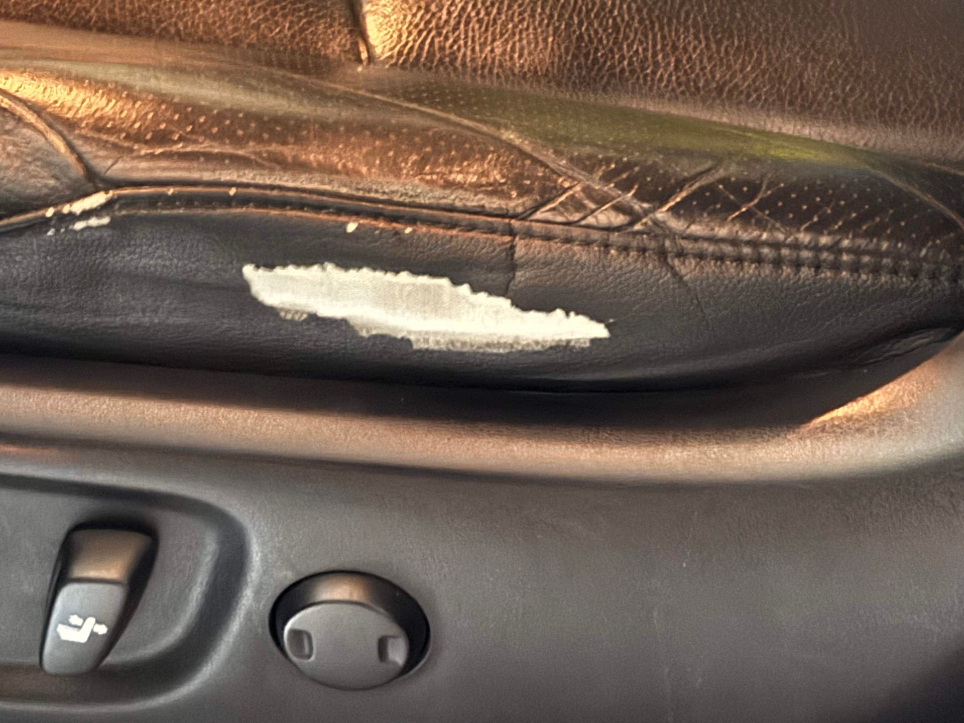 Damaged black leather car seat with peeling white material.