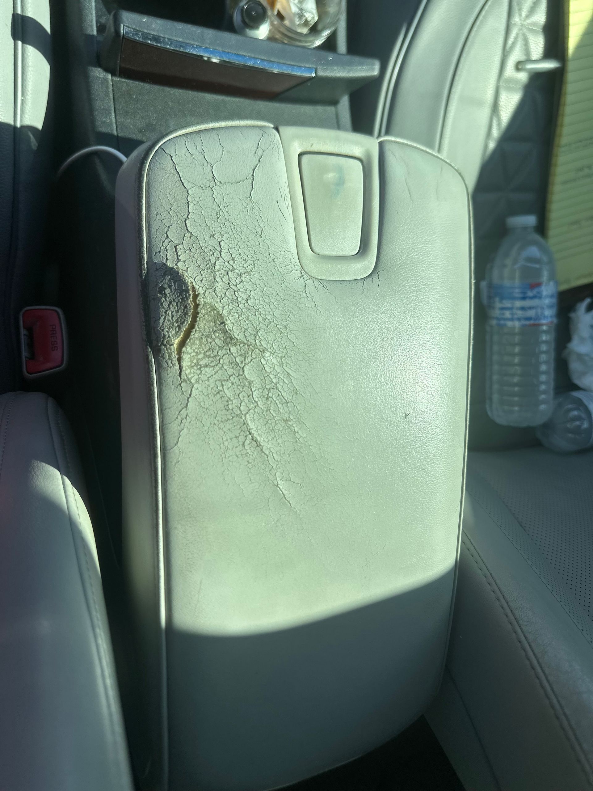 Gray car armrest with peeling upholstery and a water bottle in the background.
