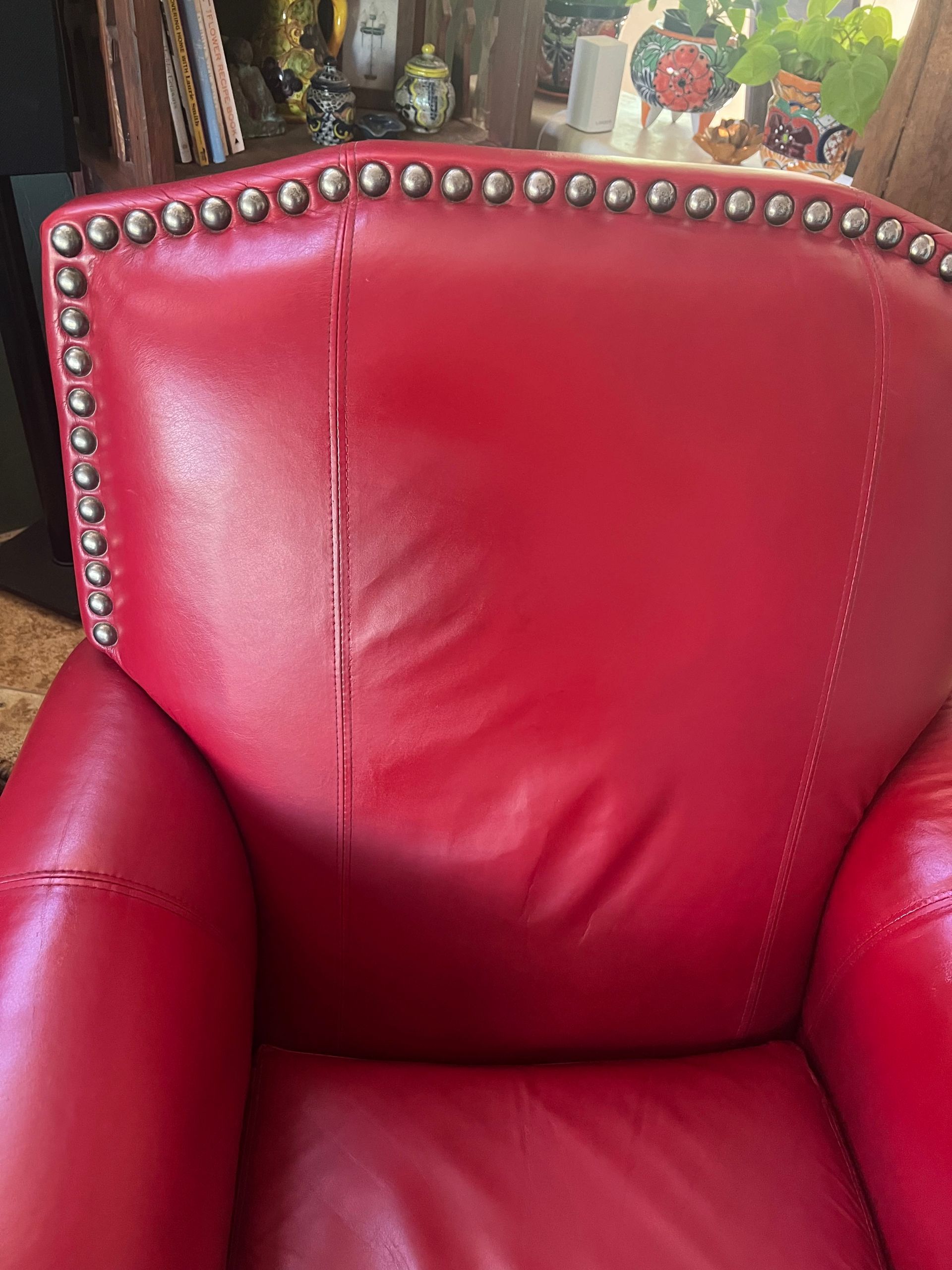 Red leather chair with silver stud trim, vertical tear in the back.