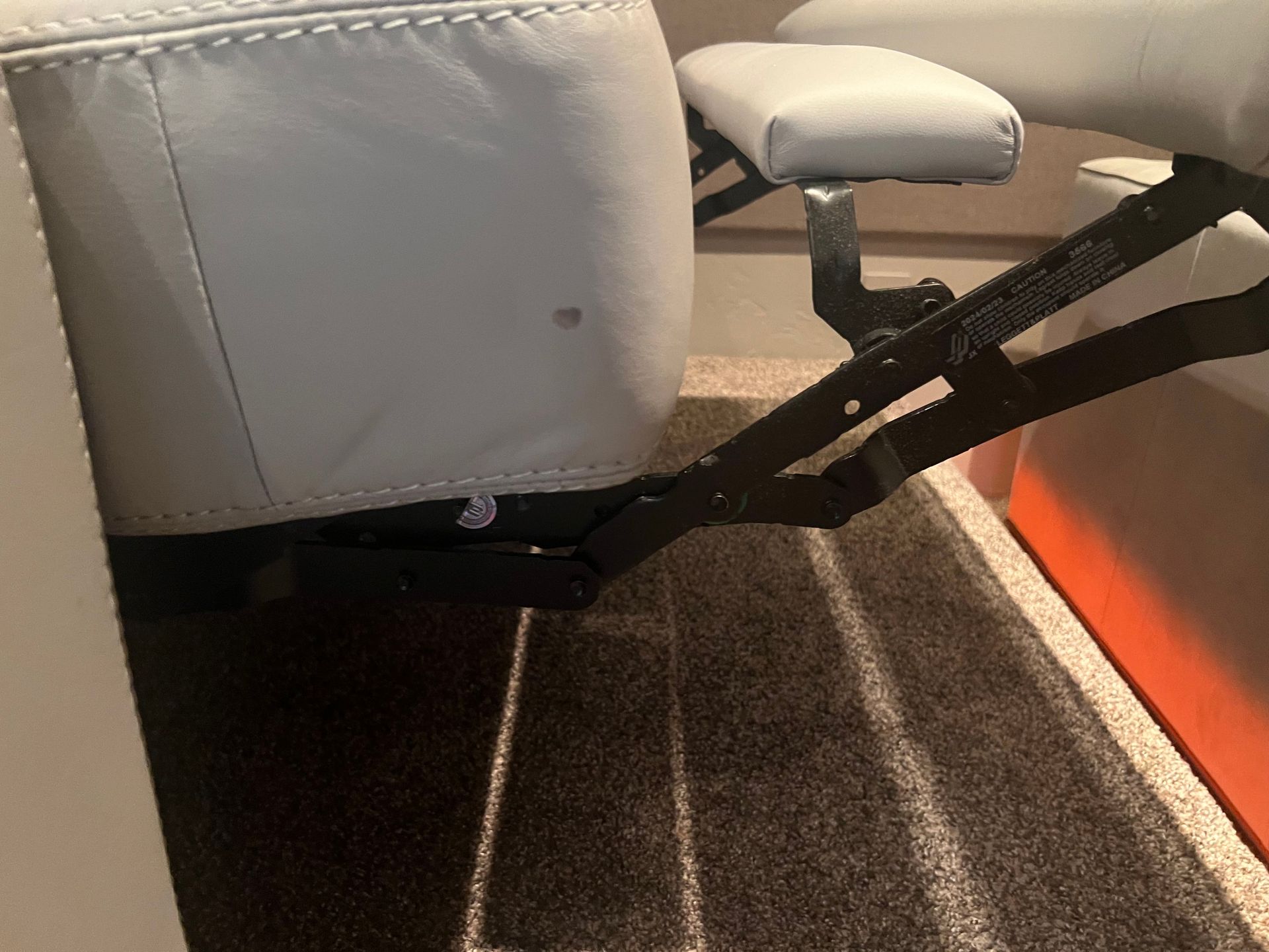 Reclining chair mechanism. Black metal frame supporting gray leather seat and armrest on a carpeted floor.