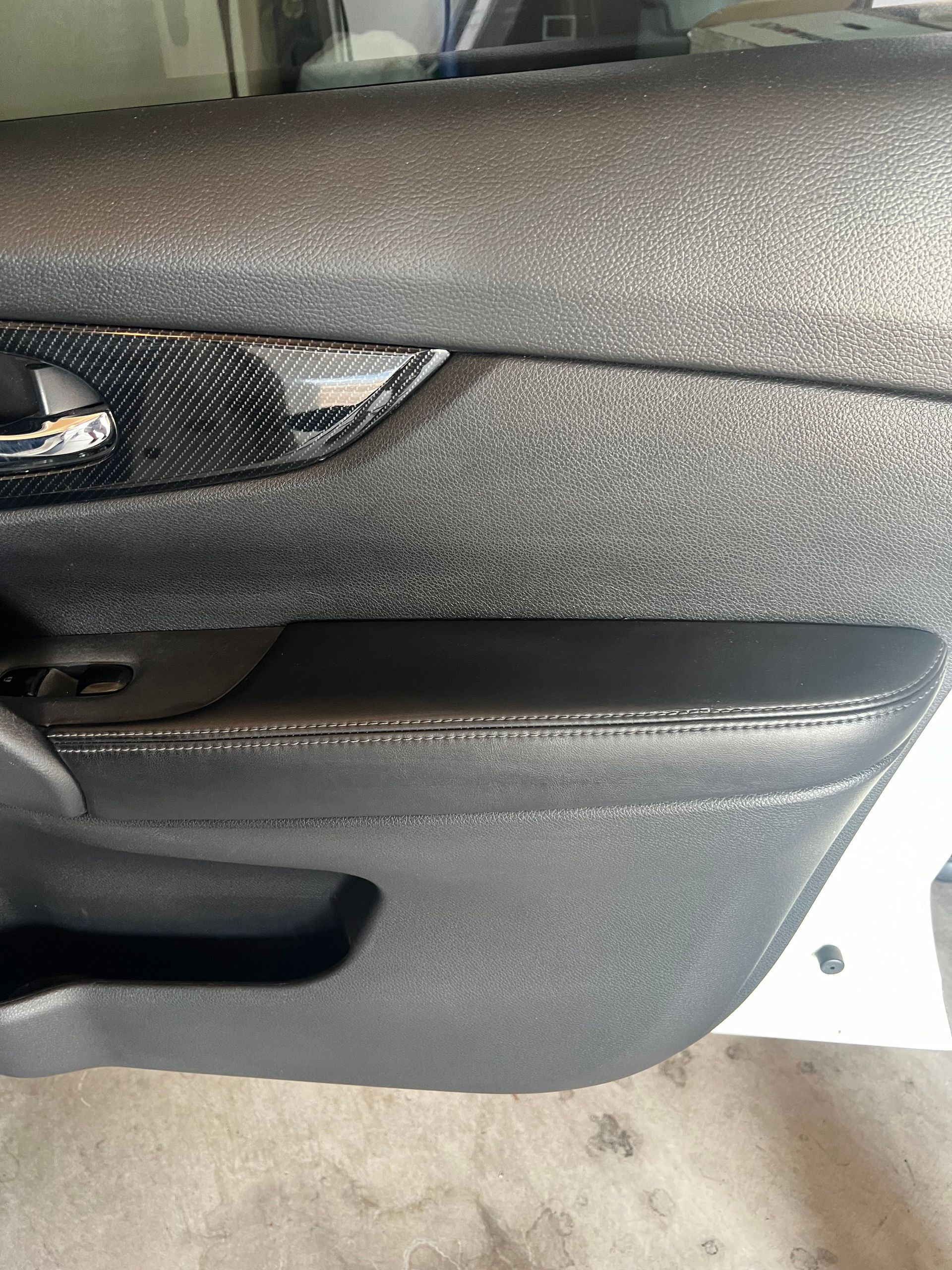 Car door interior, textured black plastic with silver flecks, black carbon fiber trim, and a silver handle.