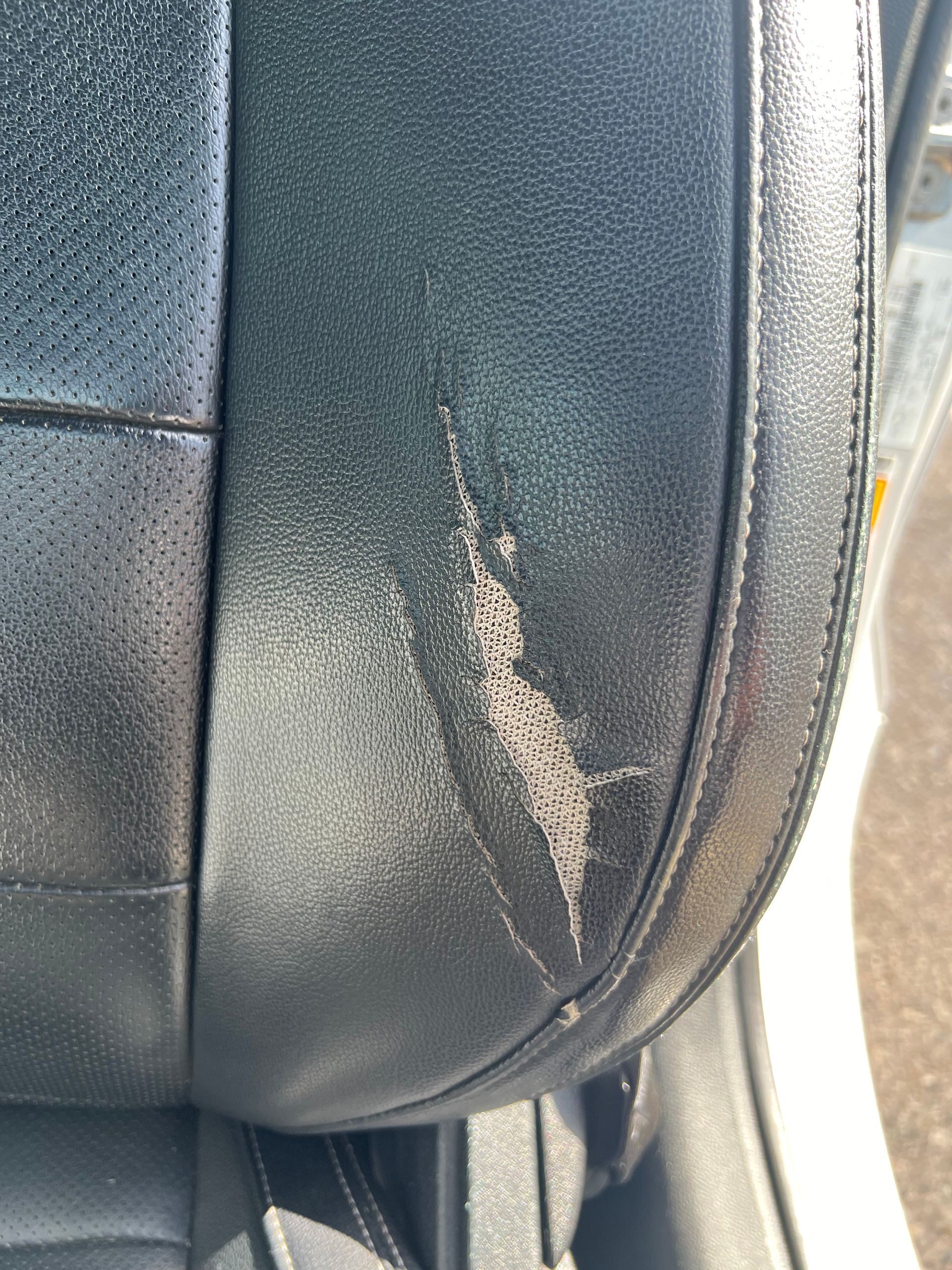 Black car seat with worn, peeling leather on the side.