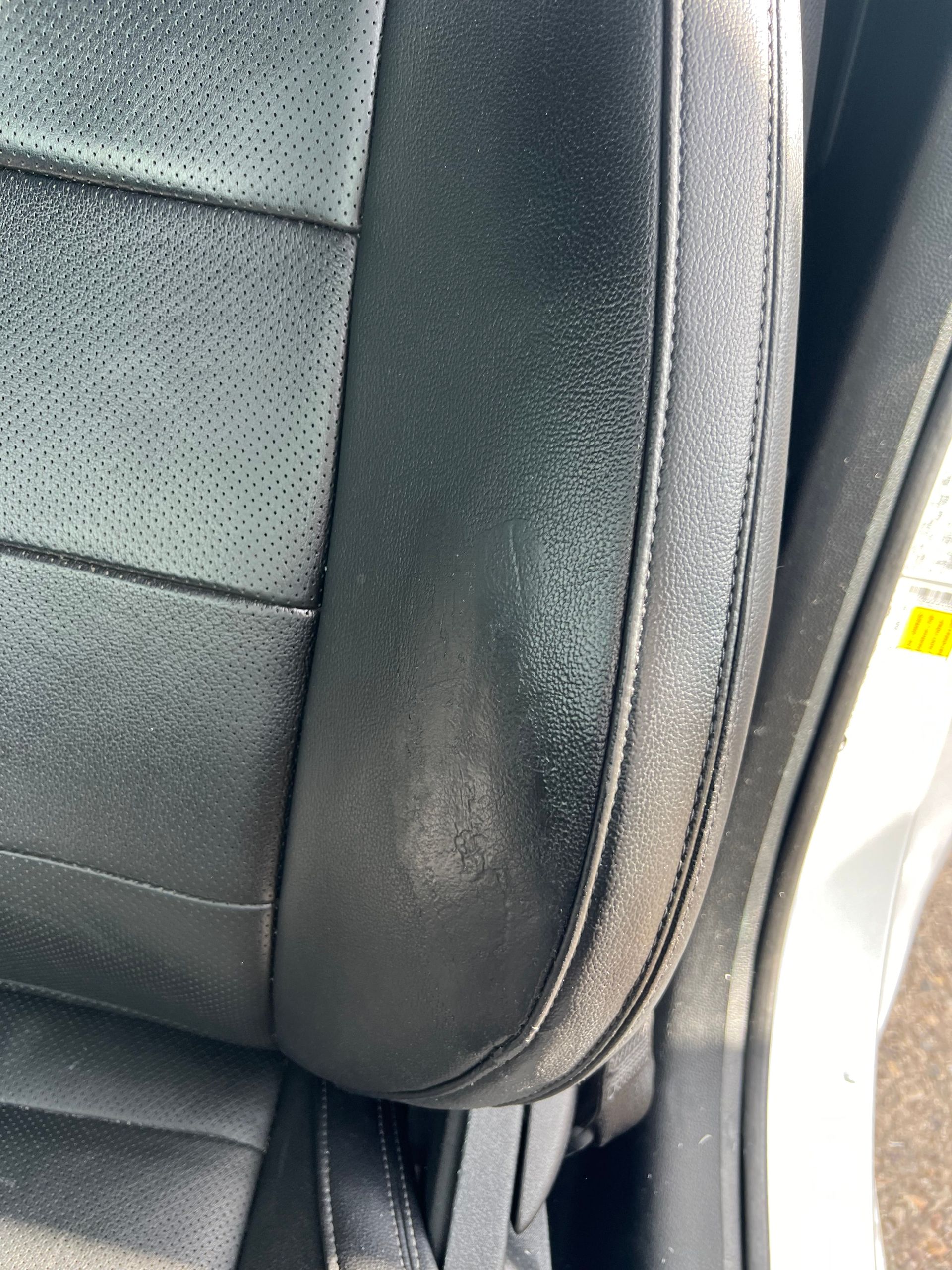 Black leather car seat with worn patch.
