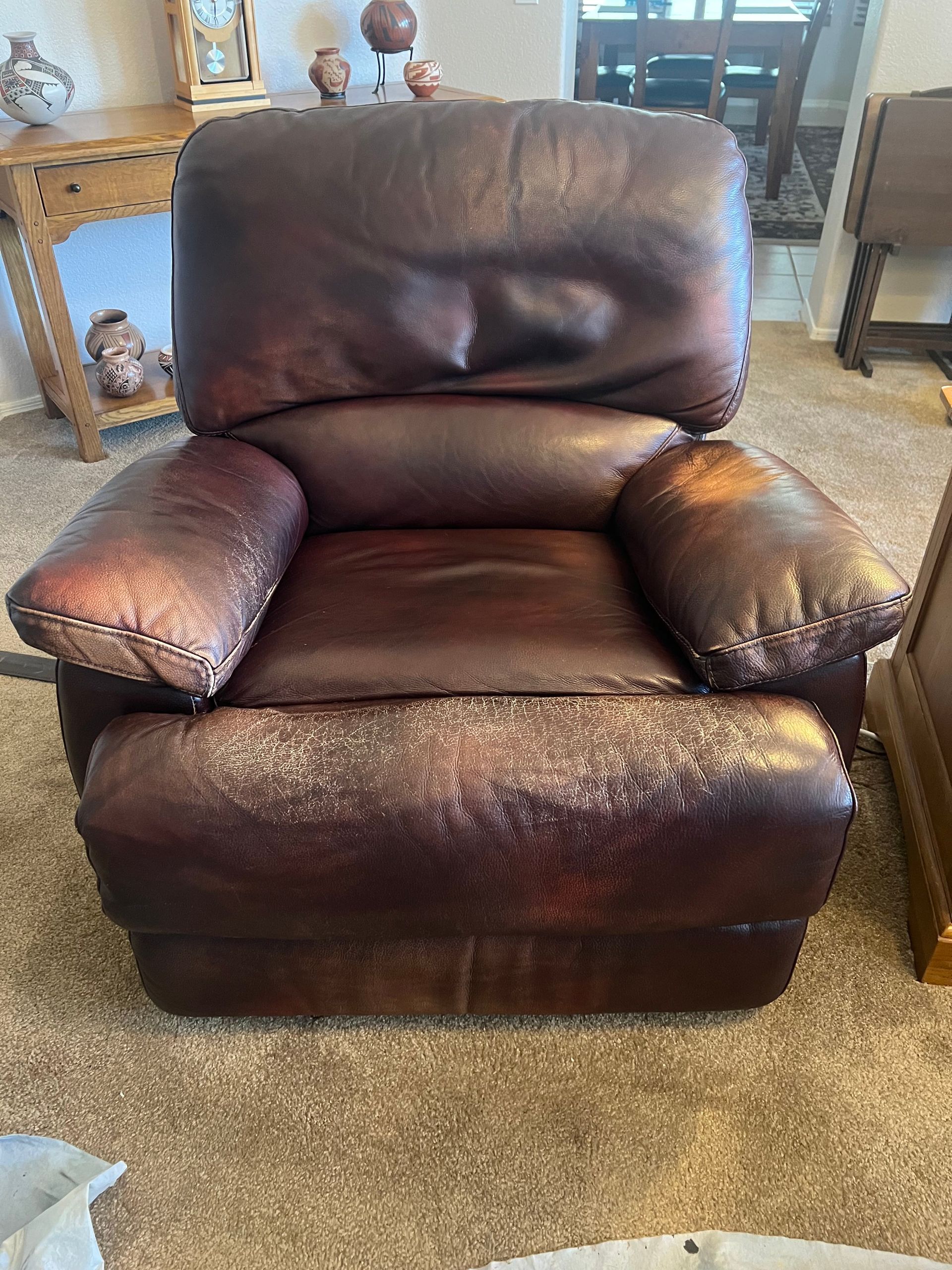 Brown leather recliner with worn patches and discoloration.