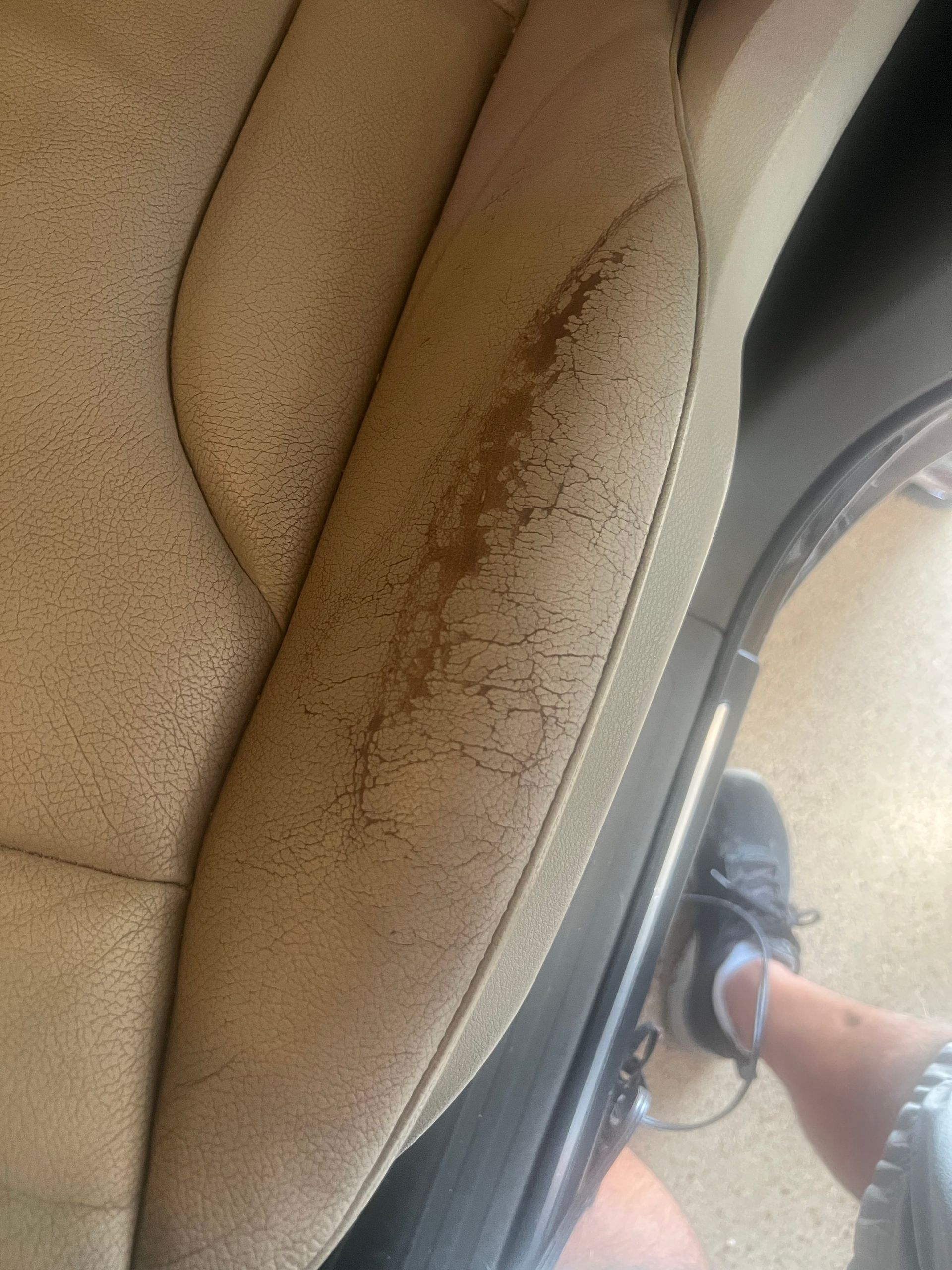 Tan car seat with cracked leather on the side. A leg and foot are visible in the corner.