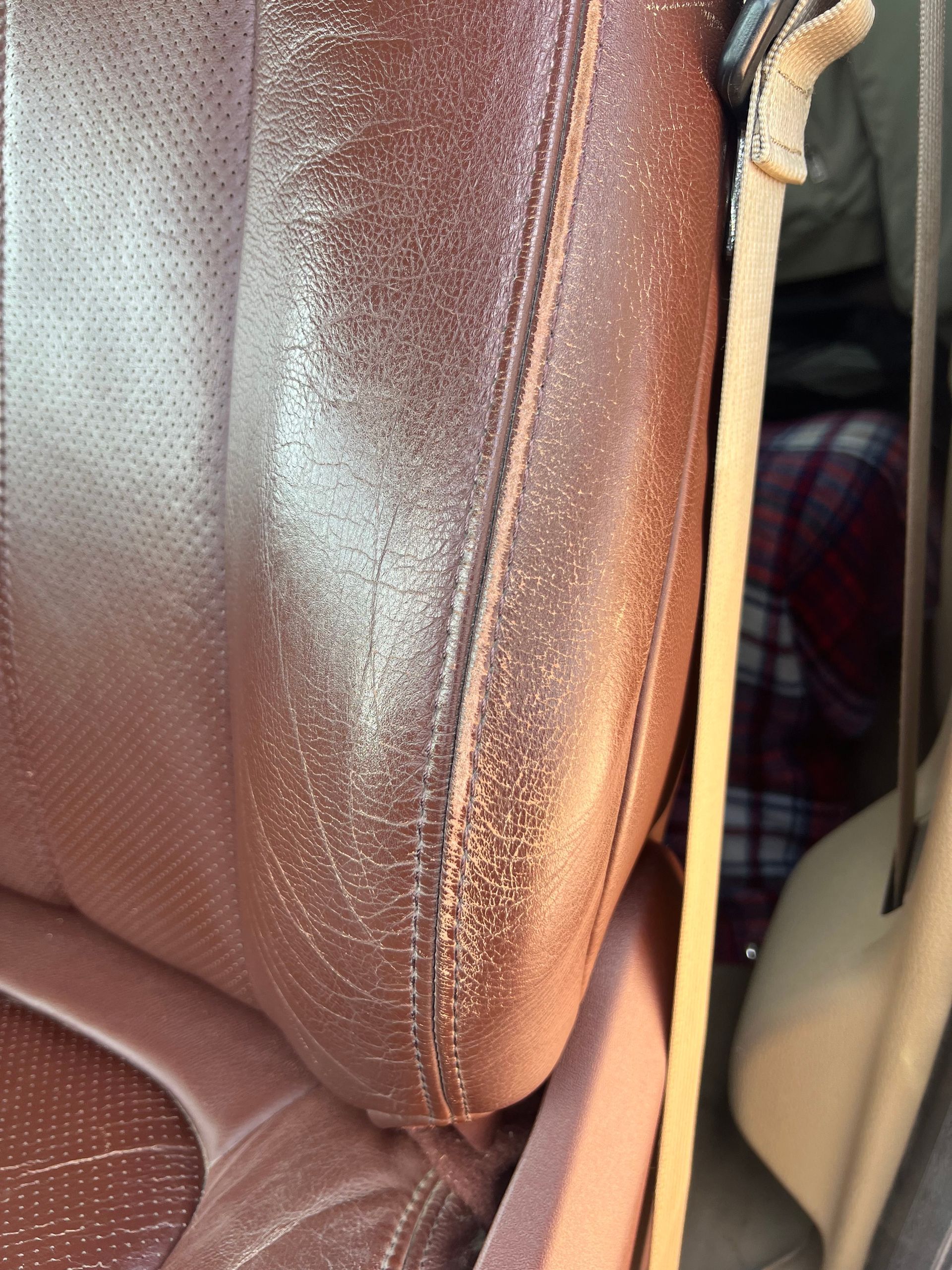 Close-up of a worn, reddish-brown leather car seat with visible cracking and wear.
