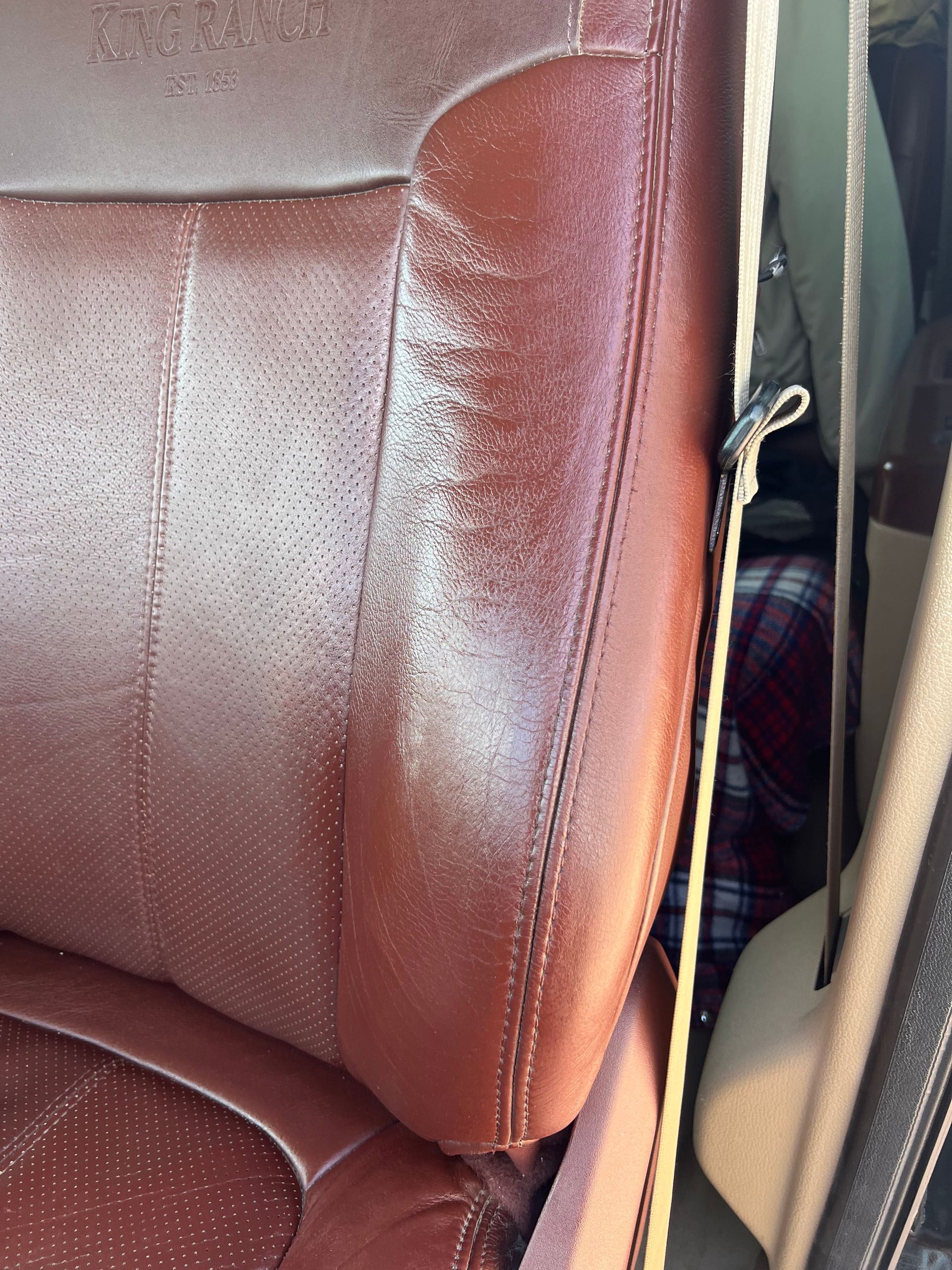Brown leather car seat with visible wear, next to a seatbelt.