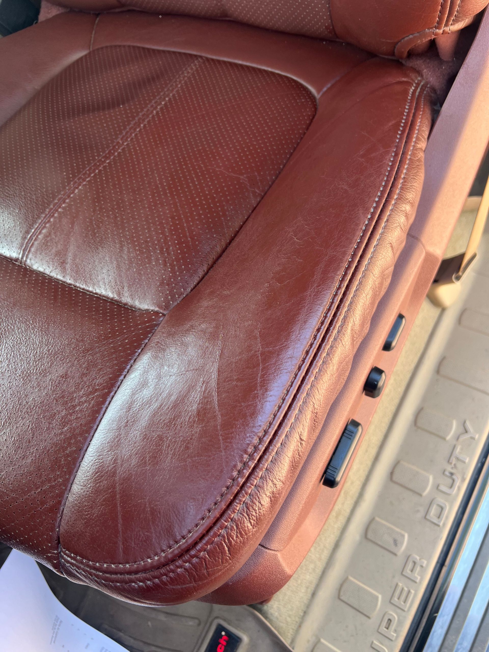 Close-up of a worn, reddish-brown leather car seat with visible creases and wear, near a power seat control.