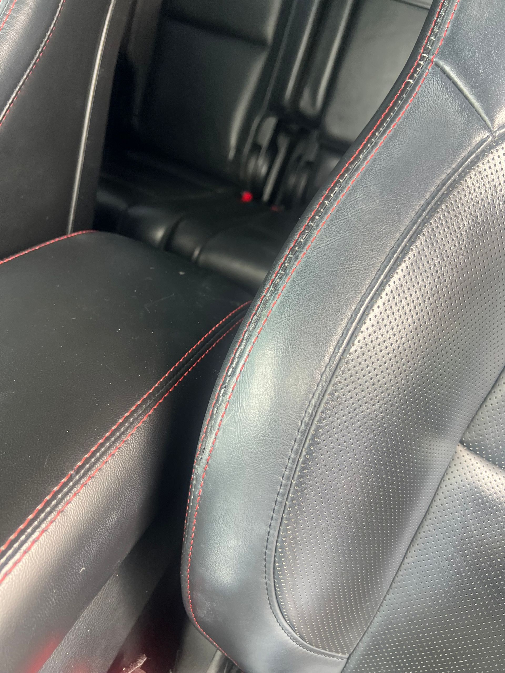 Black leather car seats with red stitching; interior view.