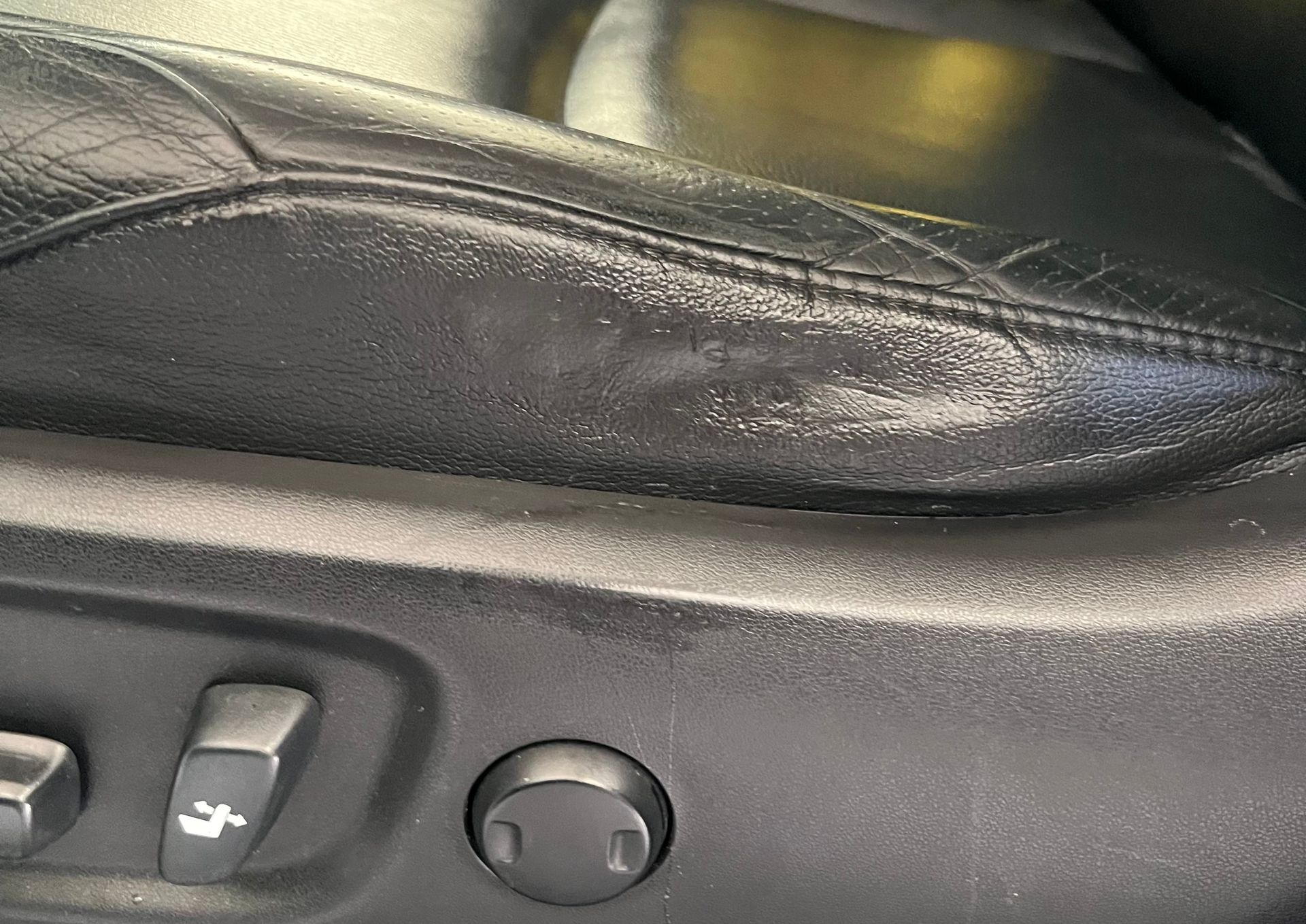 Black leather car seat with wear and tear, showing seat adjustment controls.
