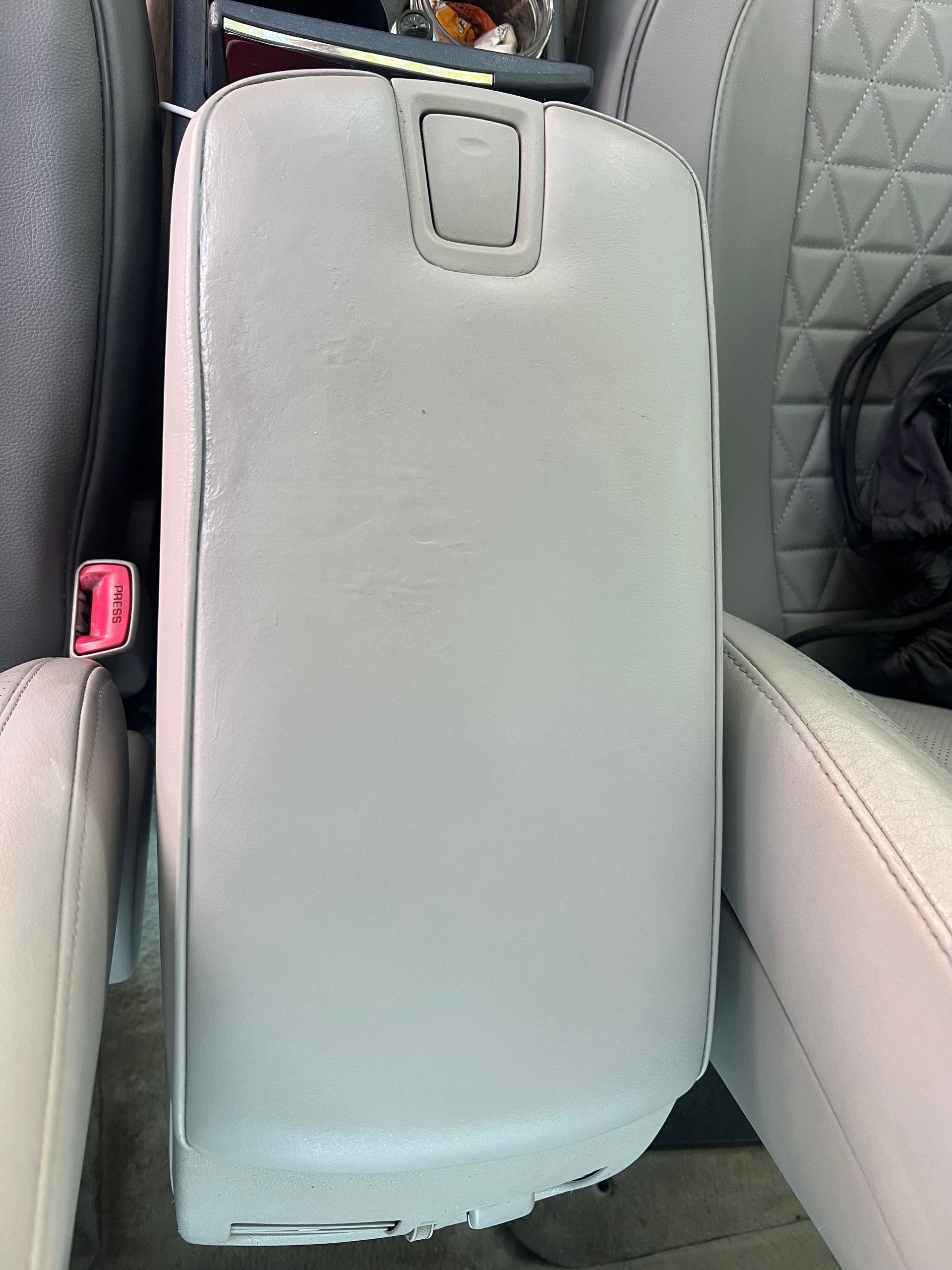 Gray car center console between two cream-colored seats with a seatbelt visible.