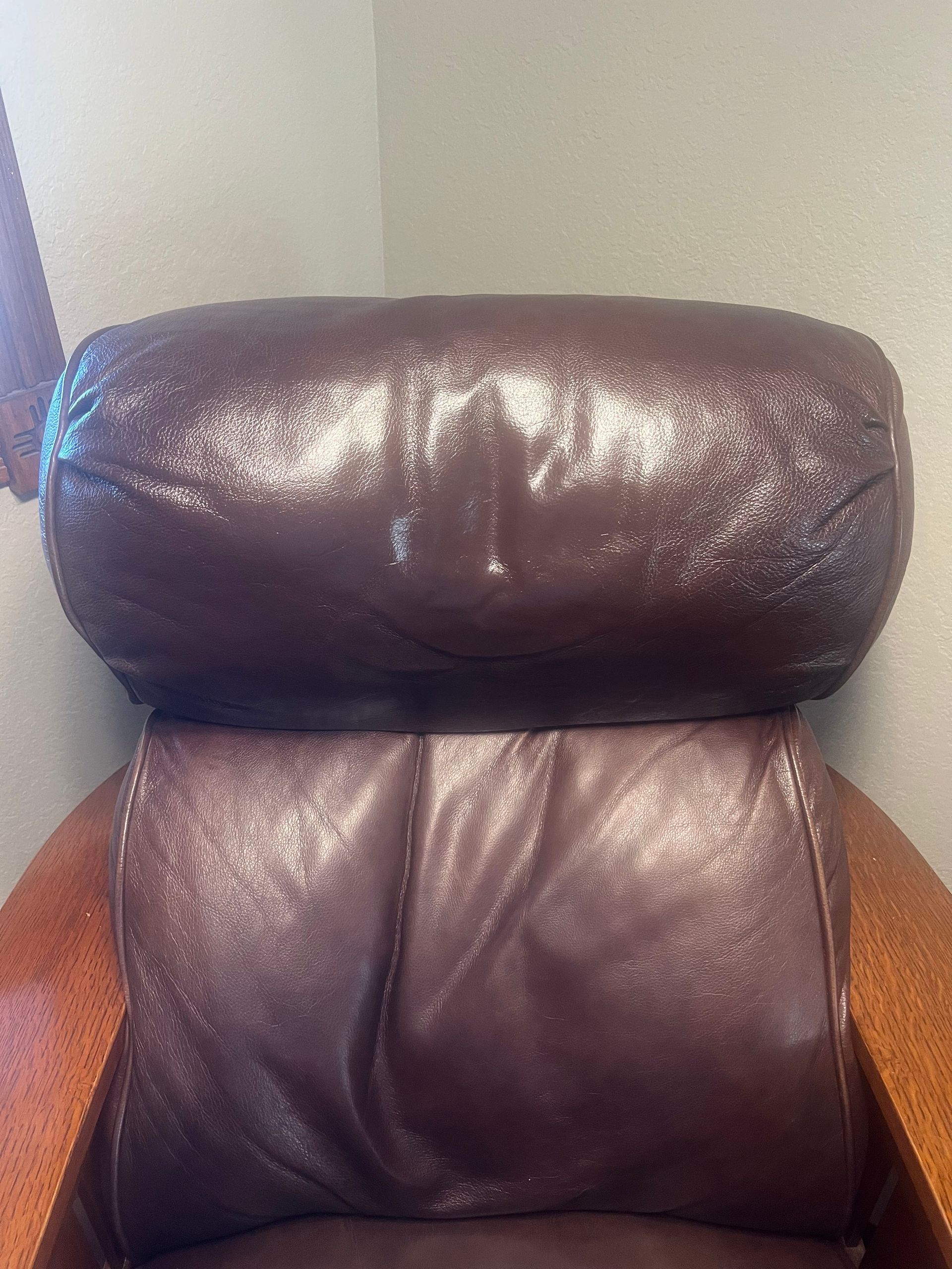 Brown leather armchair headrest with signs of wear, against a plain wall.