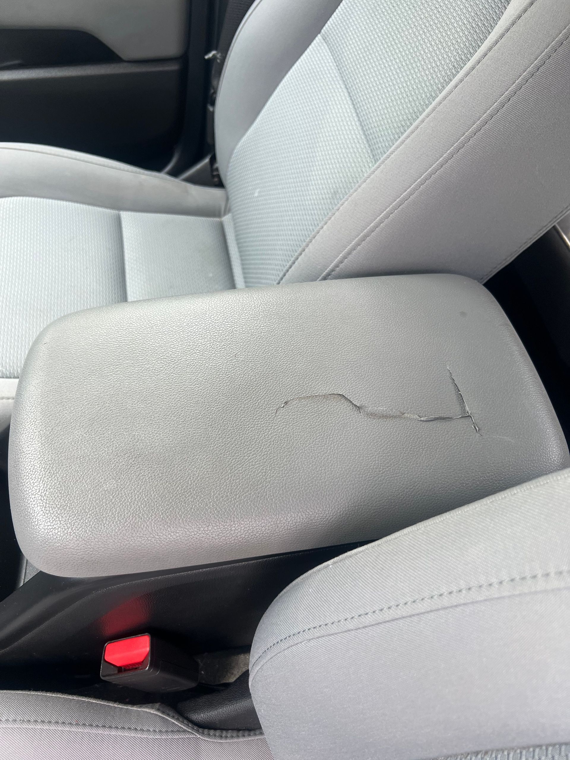 Cracked gray car console between front seats, visible seat belt buckle and armrest.
