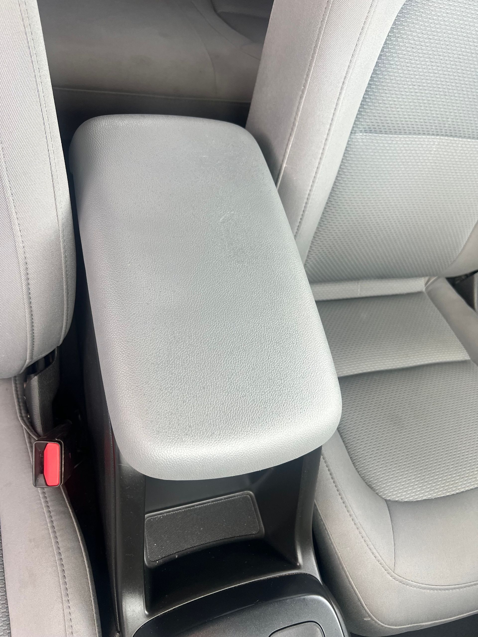 Gray car armrest between two light gray seats.
