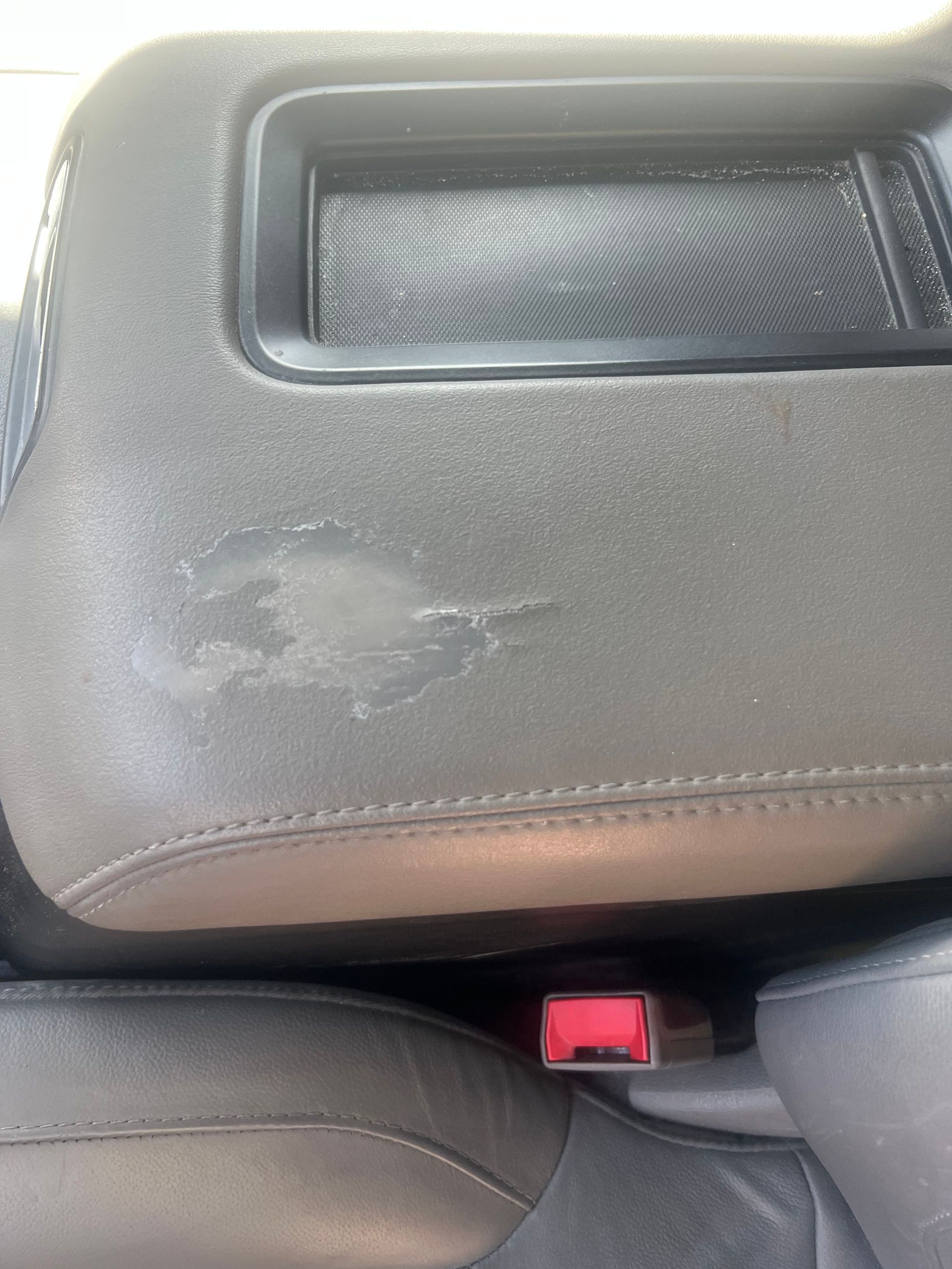 Gray car armrest with worn patch; seatbelt buckle visible below.