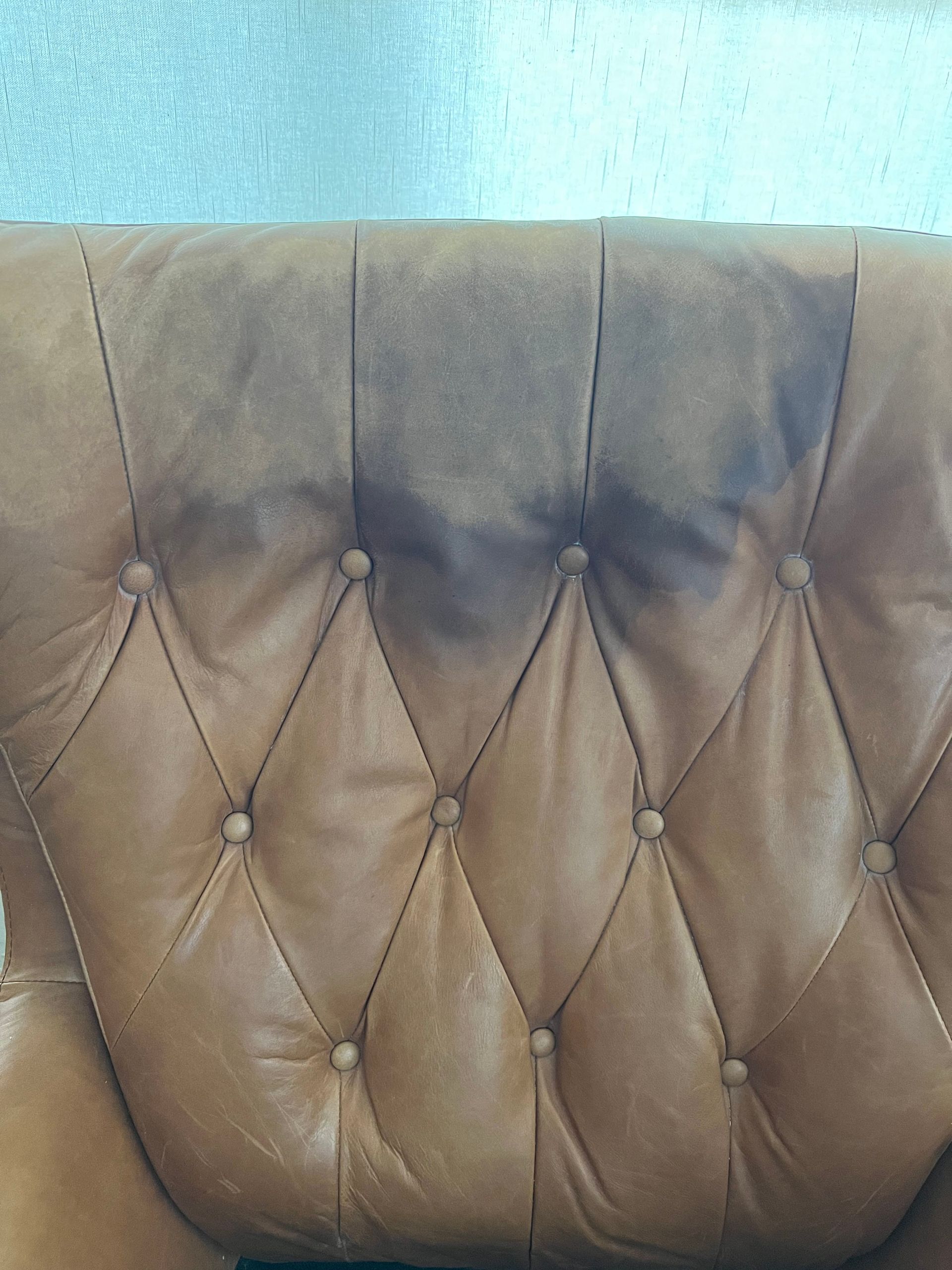 Brown leather chair back with a large, dark stain.