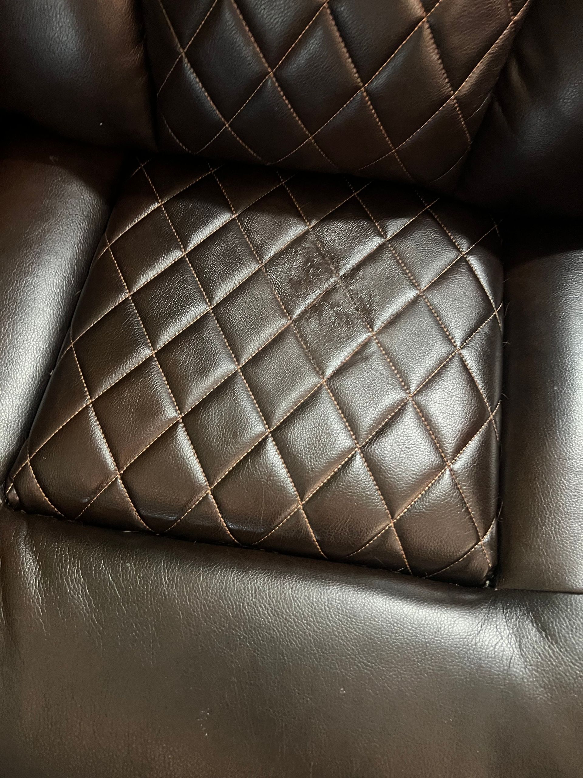 Close-up of a brown leather chair with diamond-patterned stitching.