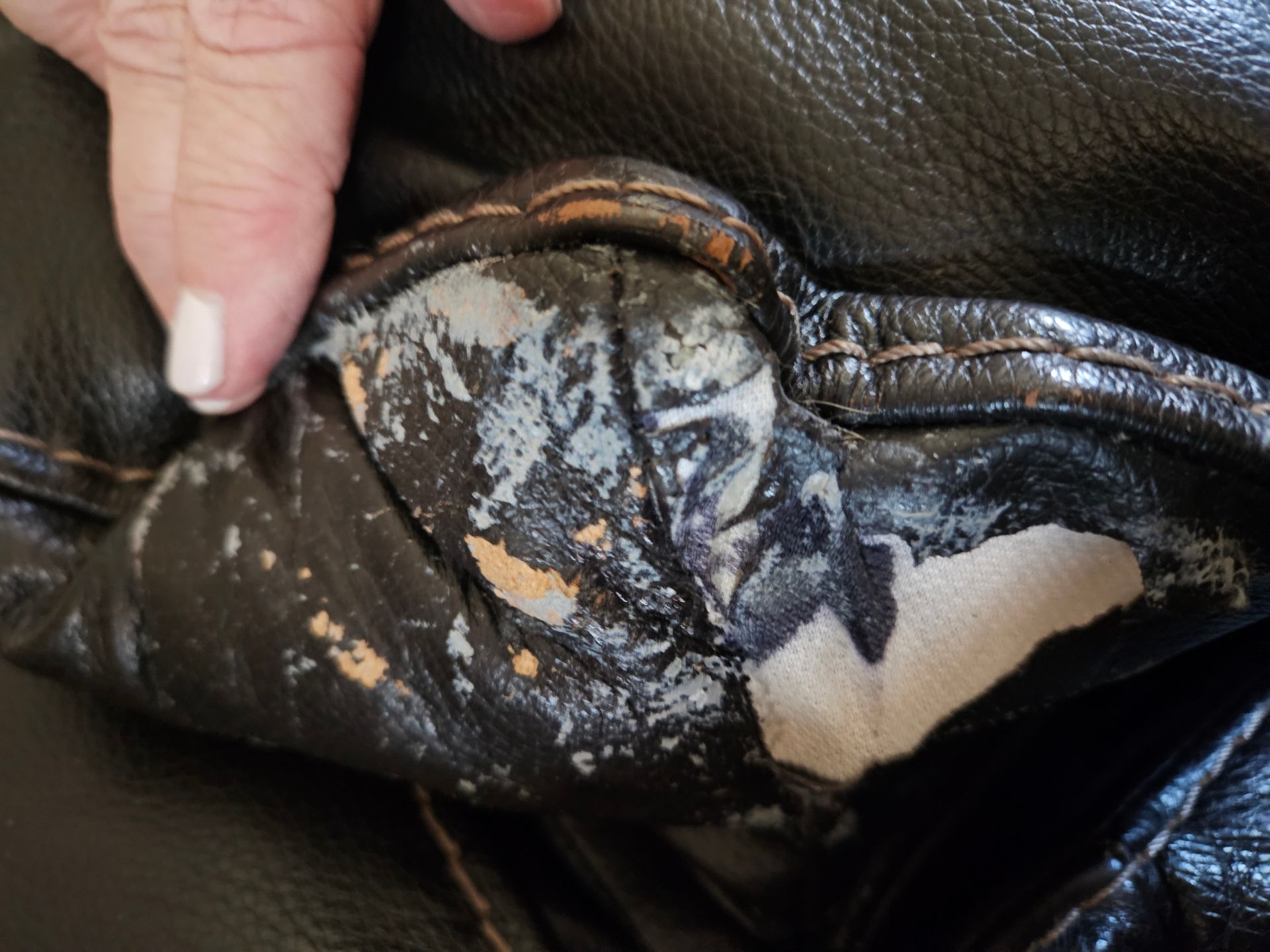 Close-up shows peeling black leather sofa with white, orange, and gray underlayment; a hand points to the damage.