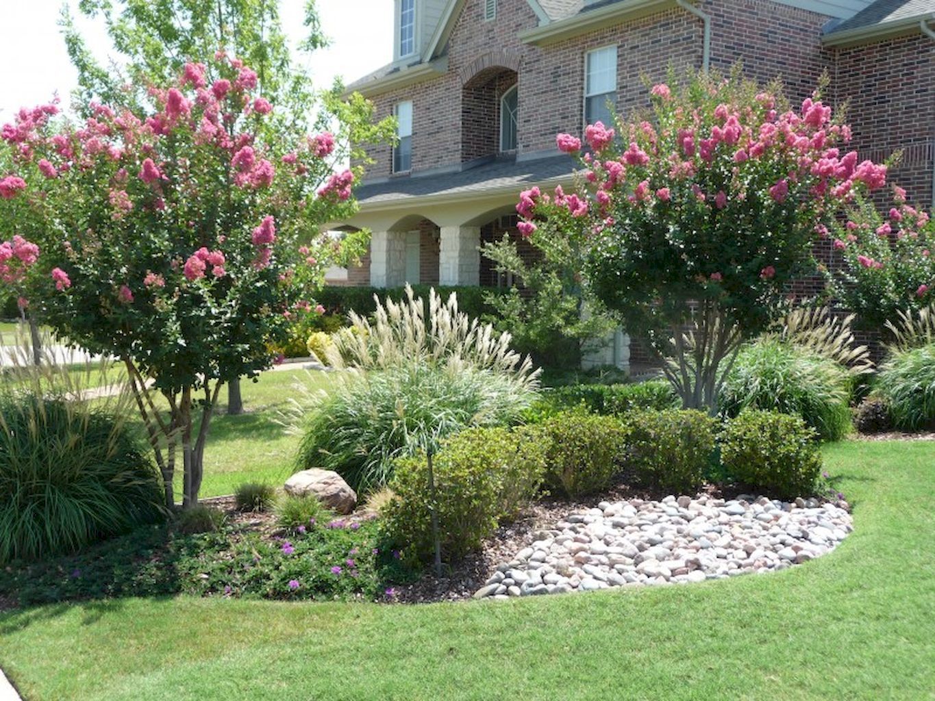 A large brick house with a lush green lawn and bushes in front of it.